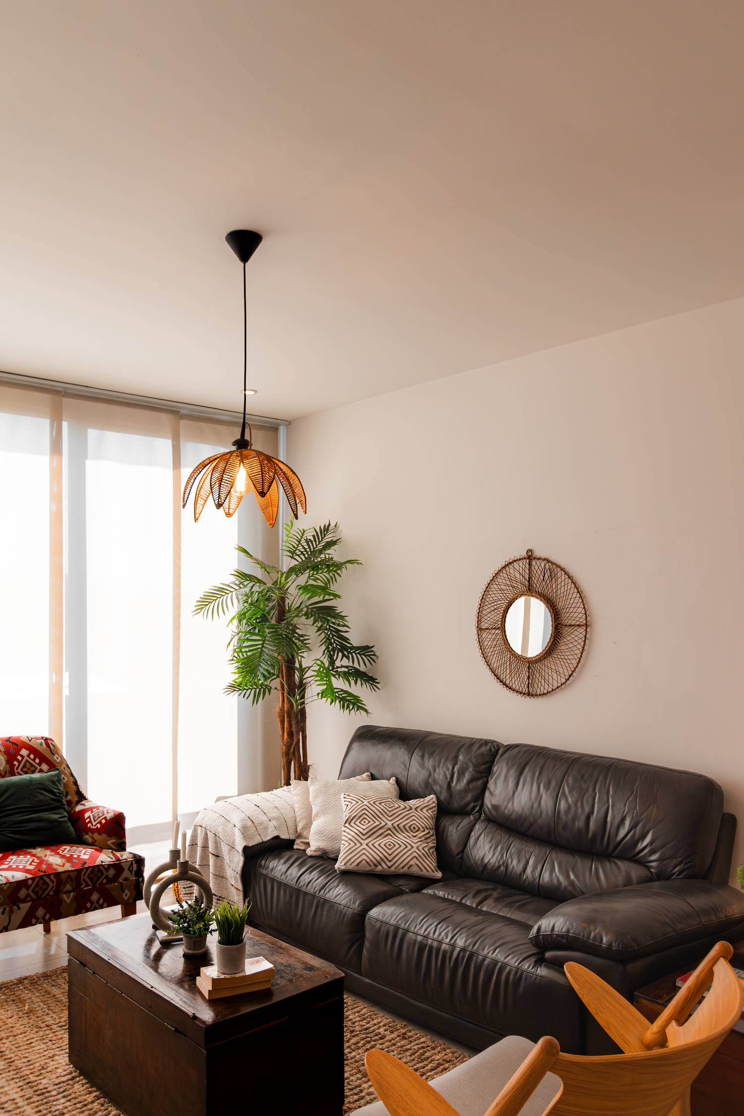 Modern living room with leather couch, decorative pendant lamp and palm plant near large windows.