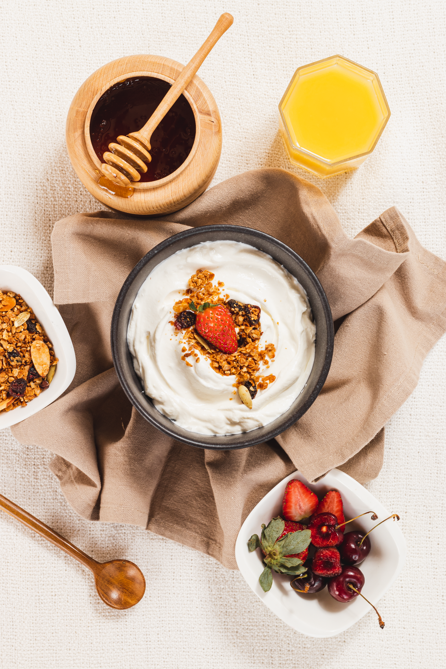 Breakfast spread with yogurt bowl, honey, orange juice and fresh berries on beige cloth.