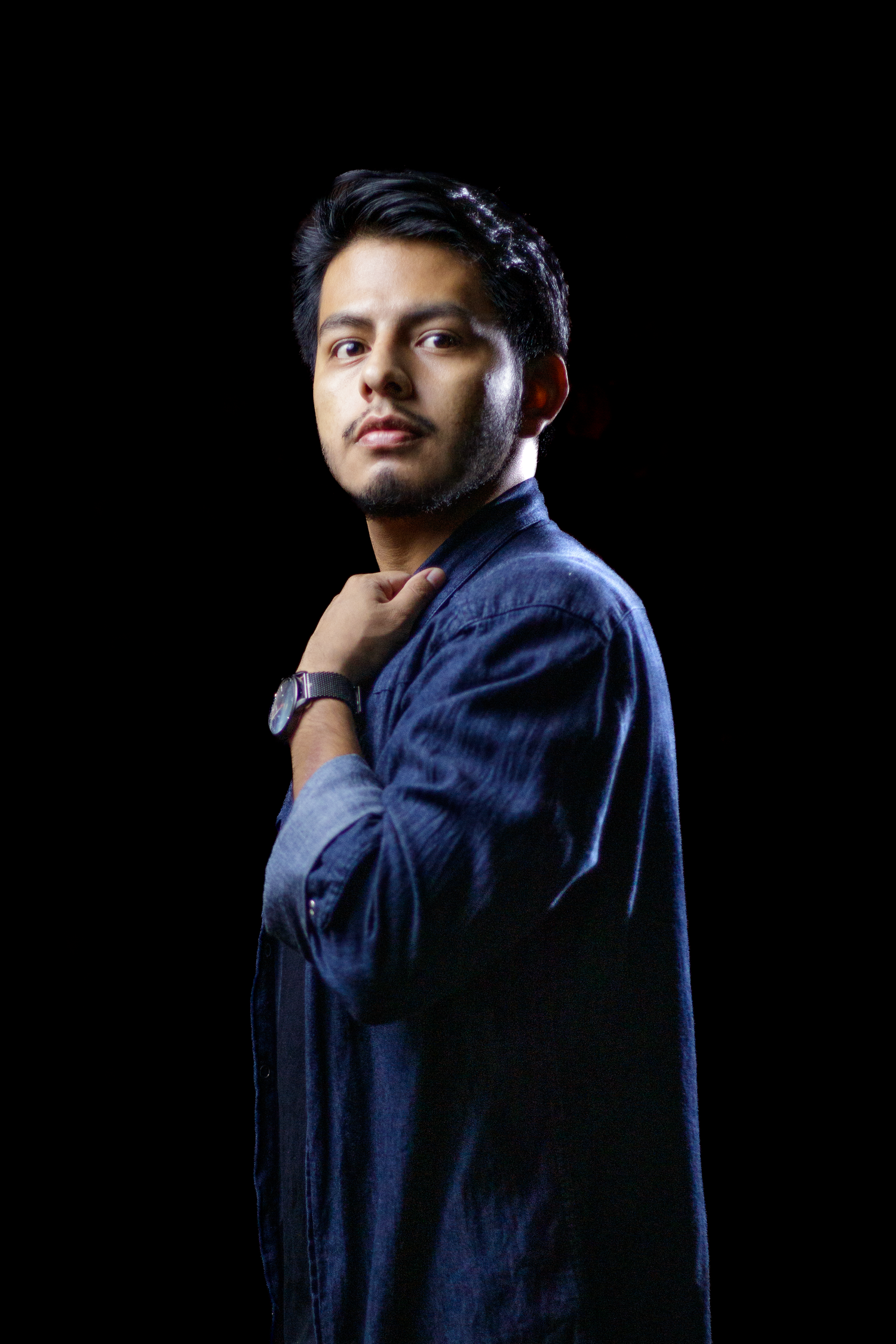 Professional portrait of a person in a navy blue shirt against a dark background with dramatic lighting.