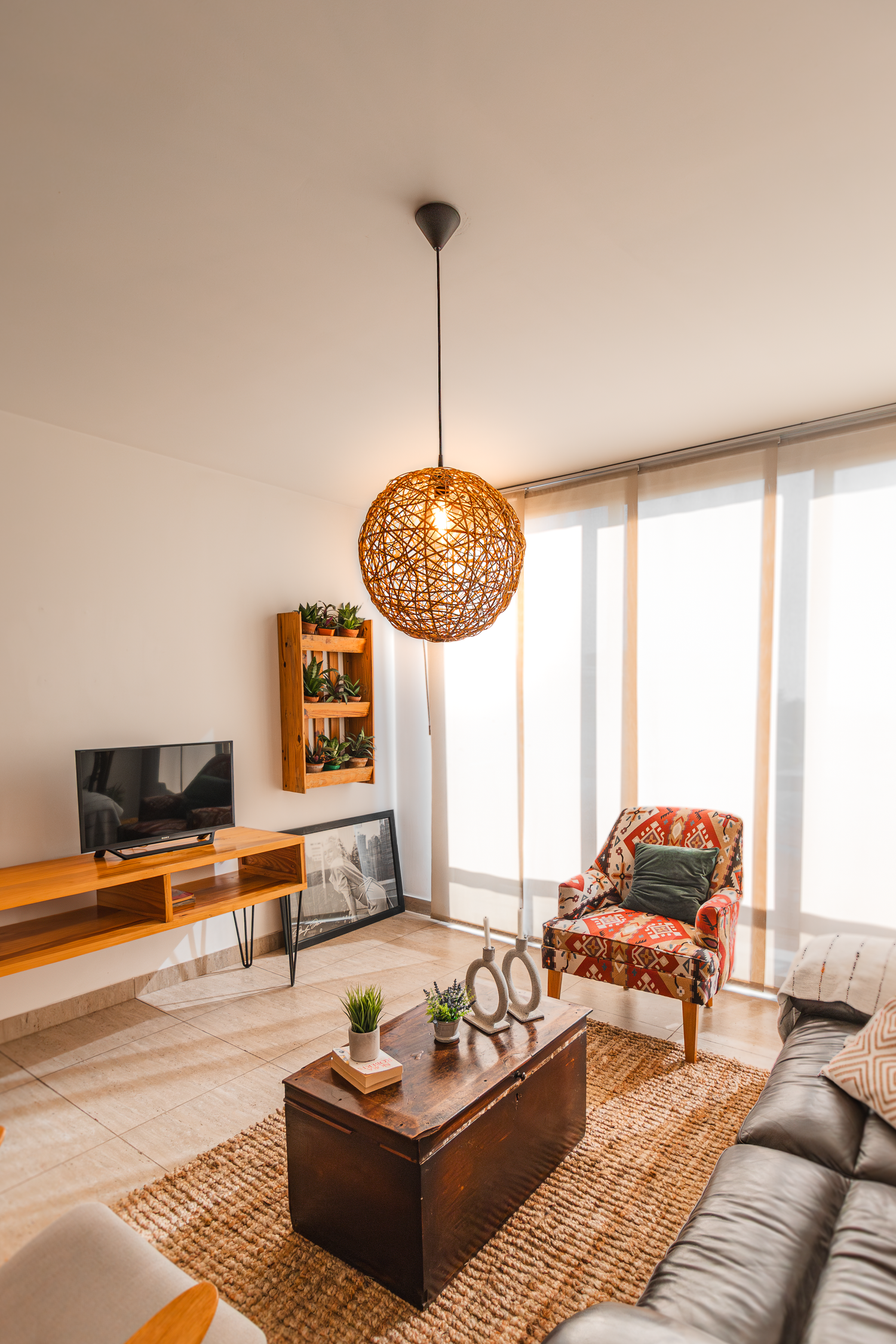Cozy living room with woven pendant light, wooden TV console, and patterned accent chair.
