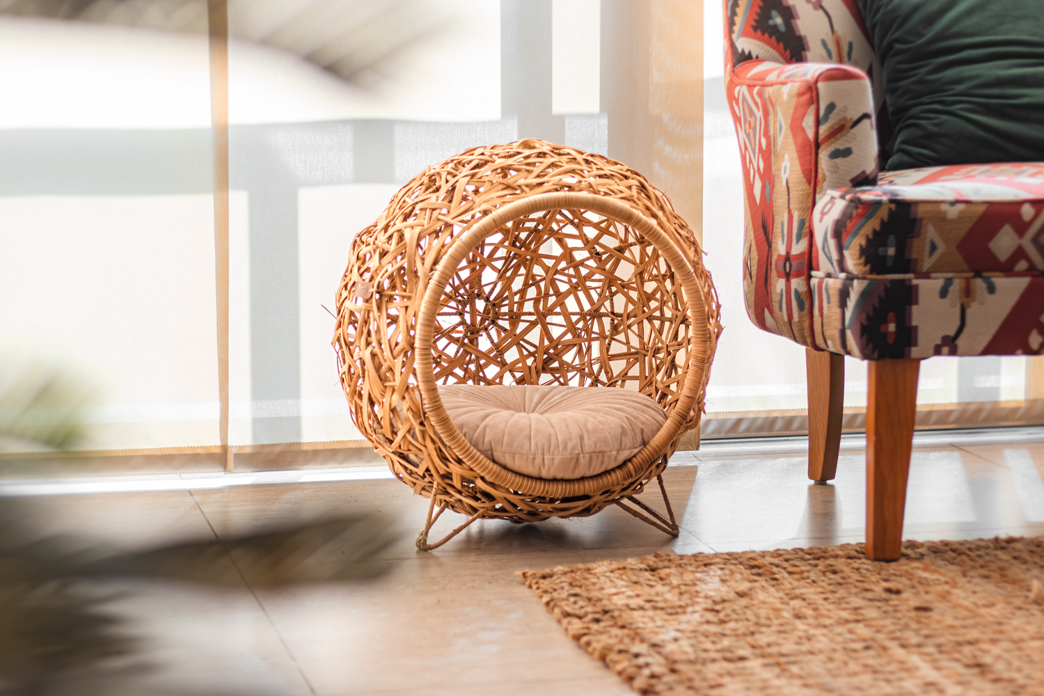 Woven rattan pod chair with cushion next to furniture on natural fiber rug.