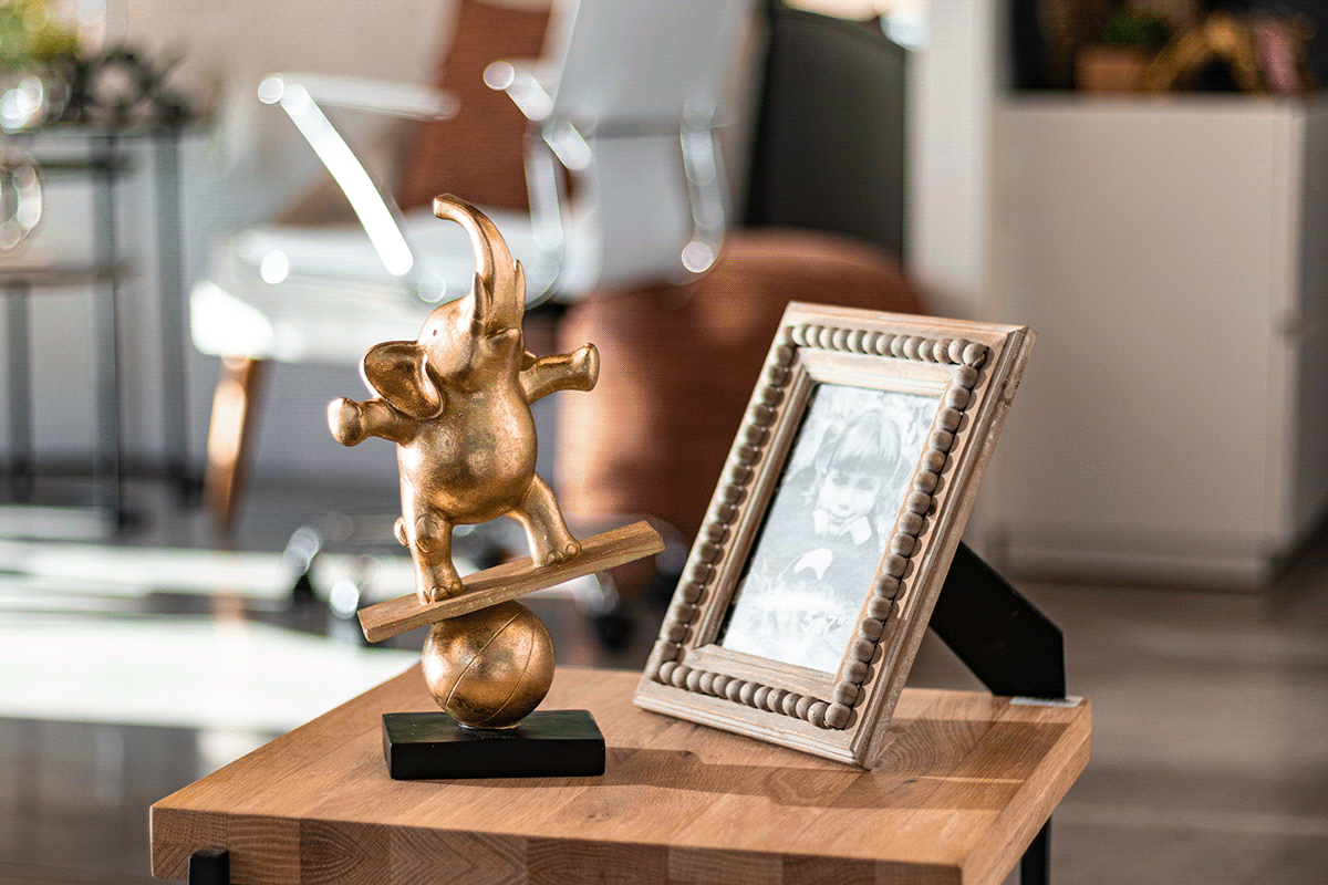 Decorative gold cherub statue and picture frame displayed on wooden table in sunlit room.