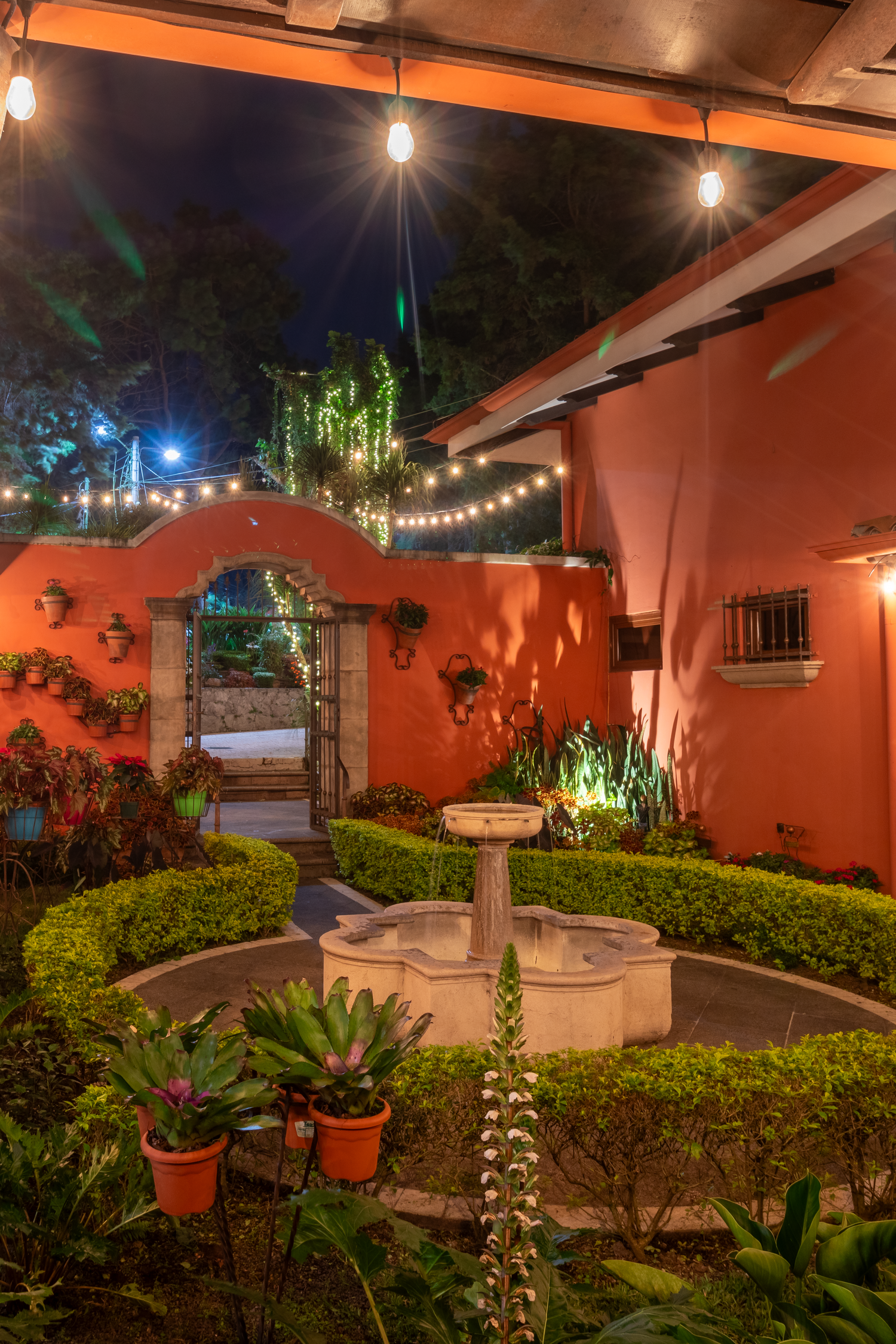 Mediterranean garden courtyard with fountain and string lights creating magical evening ambiance.