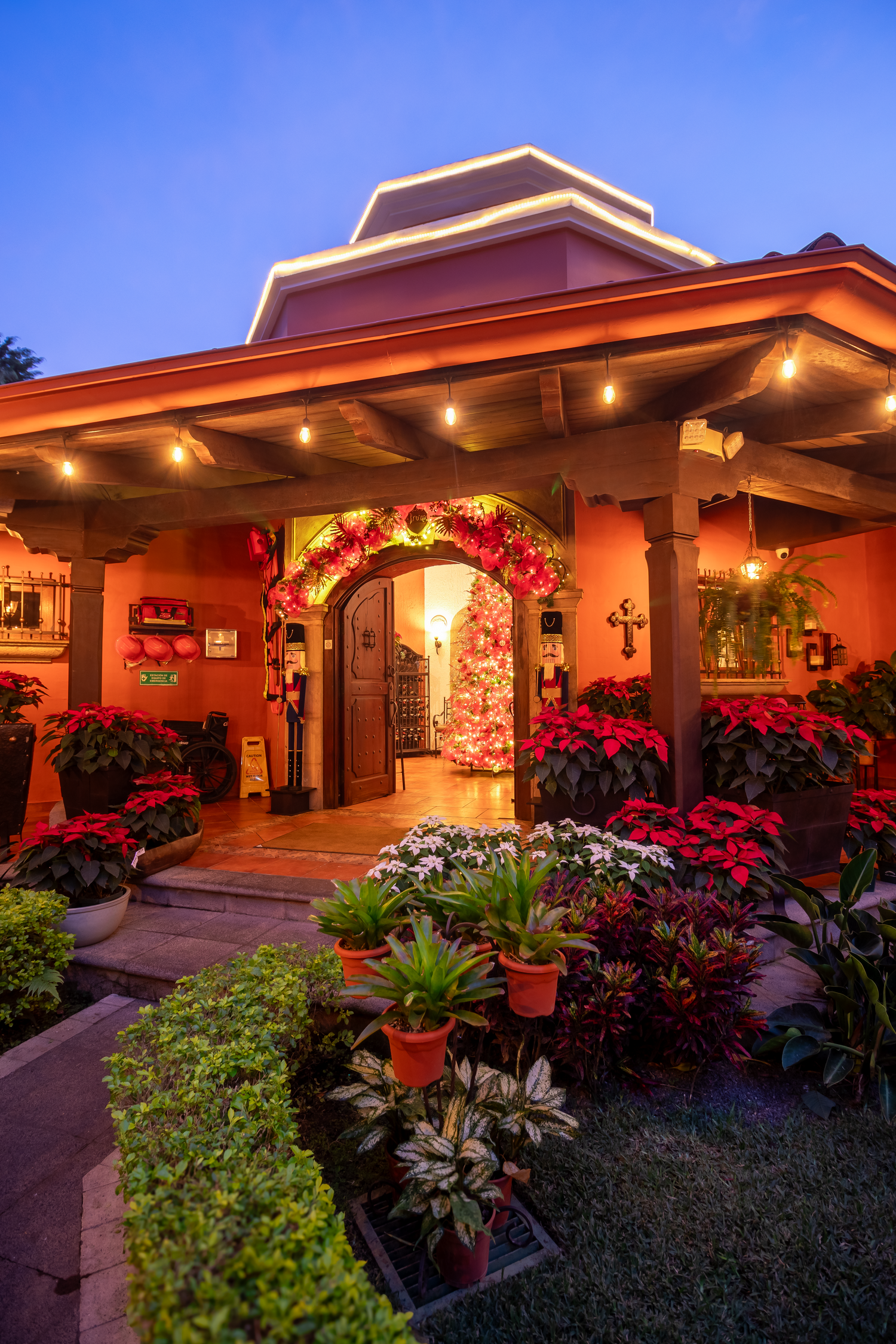 Romantic entrance to Spanish-style building with floral archway and holiday lighting at twilight.