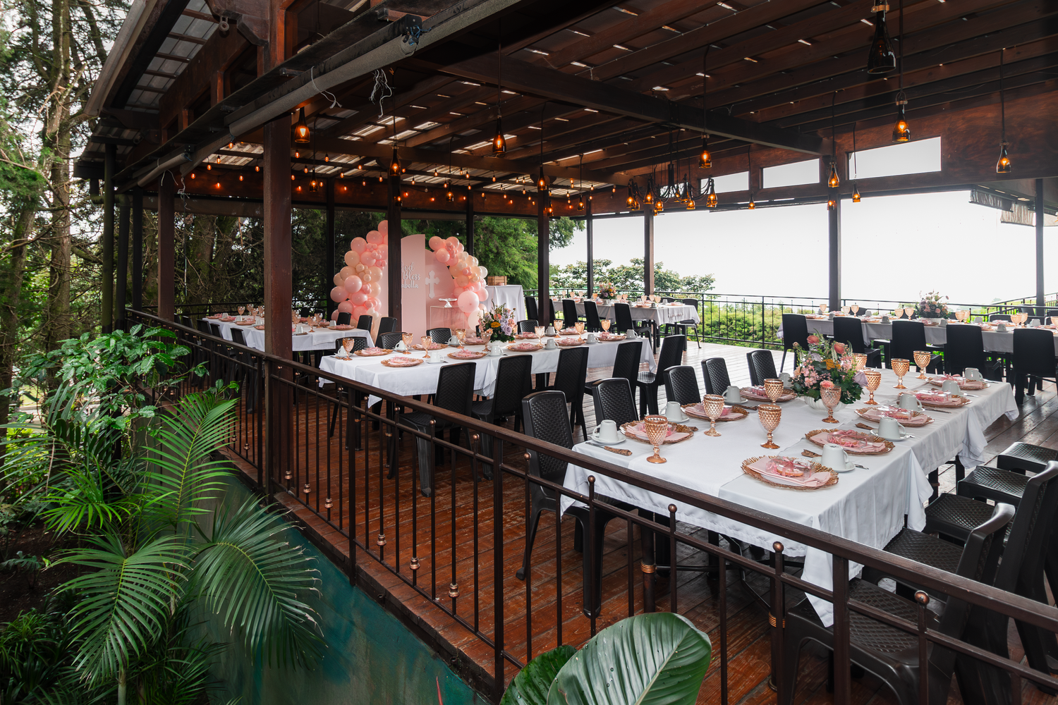 Covered restaurant patio with formal table settings and tropical greenery.