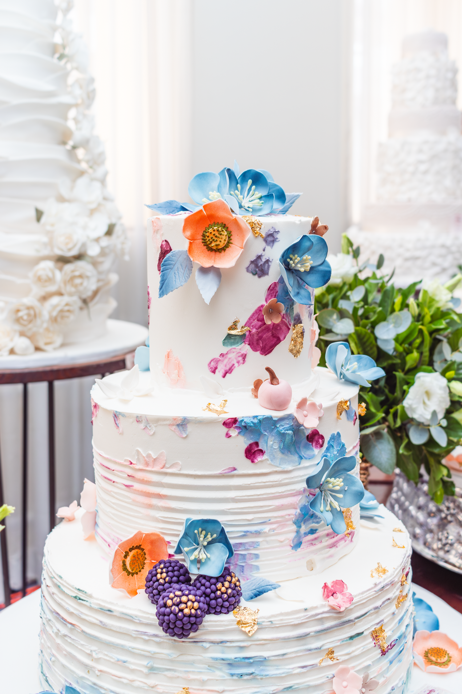 Elegant tiered wedding cake decorated with blue and pink sugar flowers on white fondant.