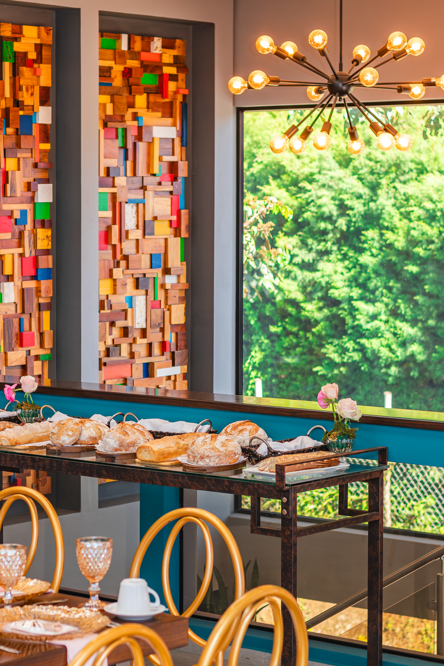 Dining room with colorful stained glass panels, modern chandelier and buffet setup.