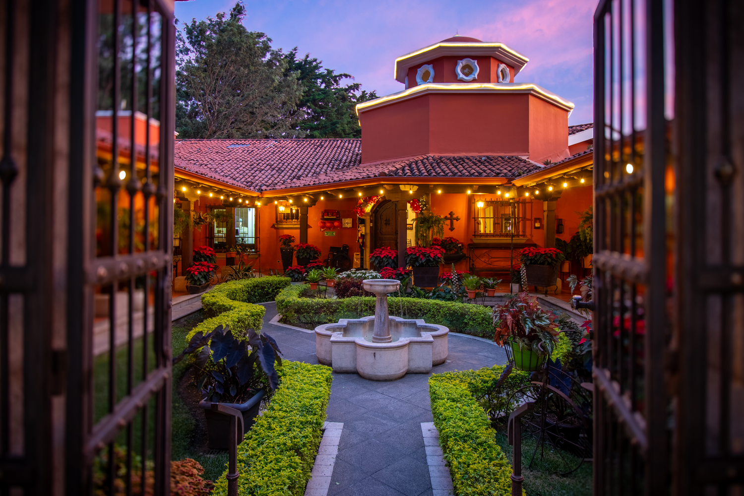 Spanish colonial courtyard with terracotta roof and central fountain illuminated at dusk.