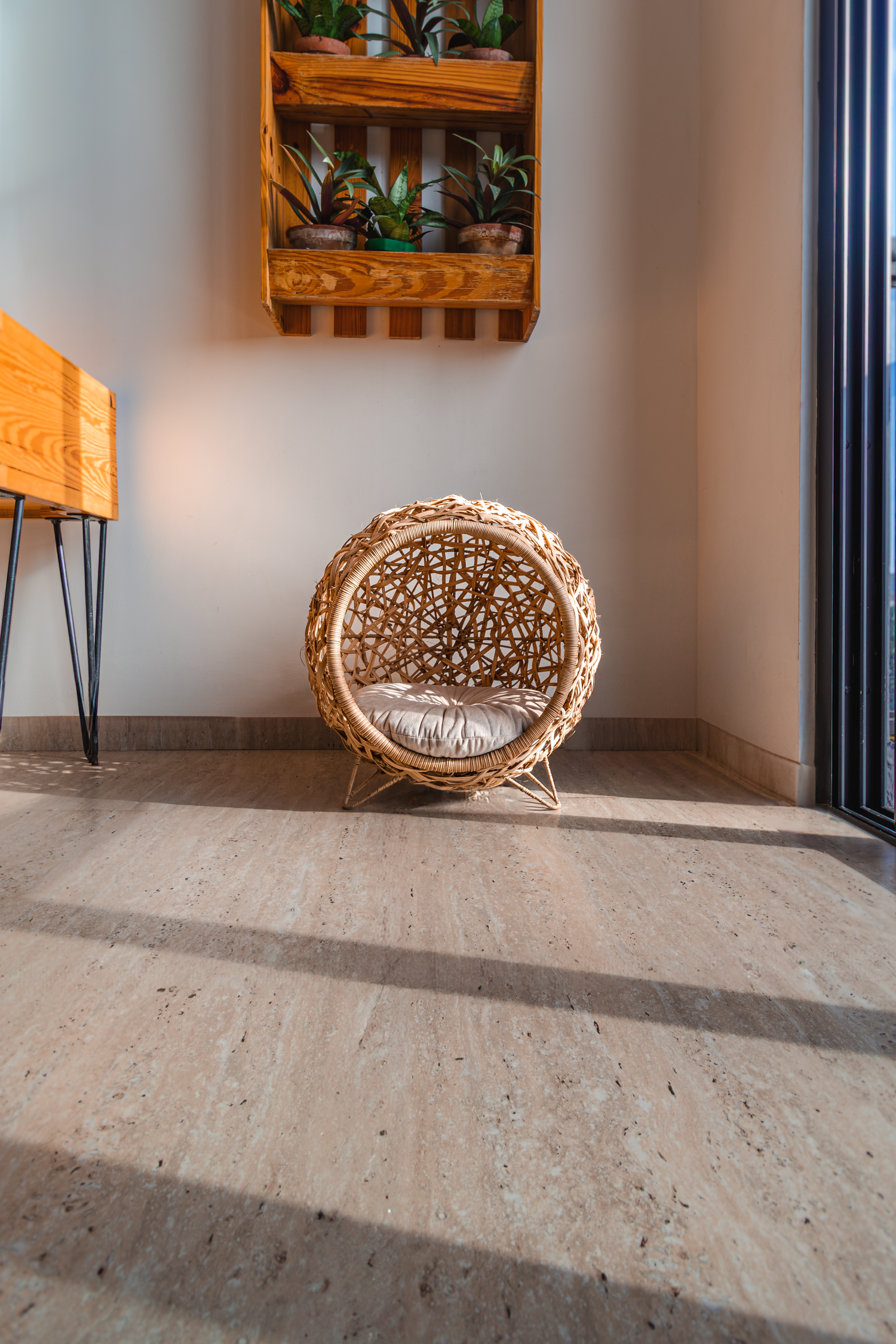 Round woven rattan chair with cushion in minimalist corner setting with wall-mounted plant shelf.