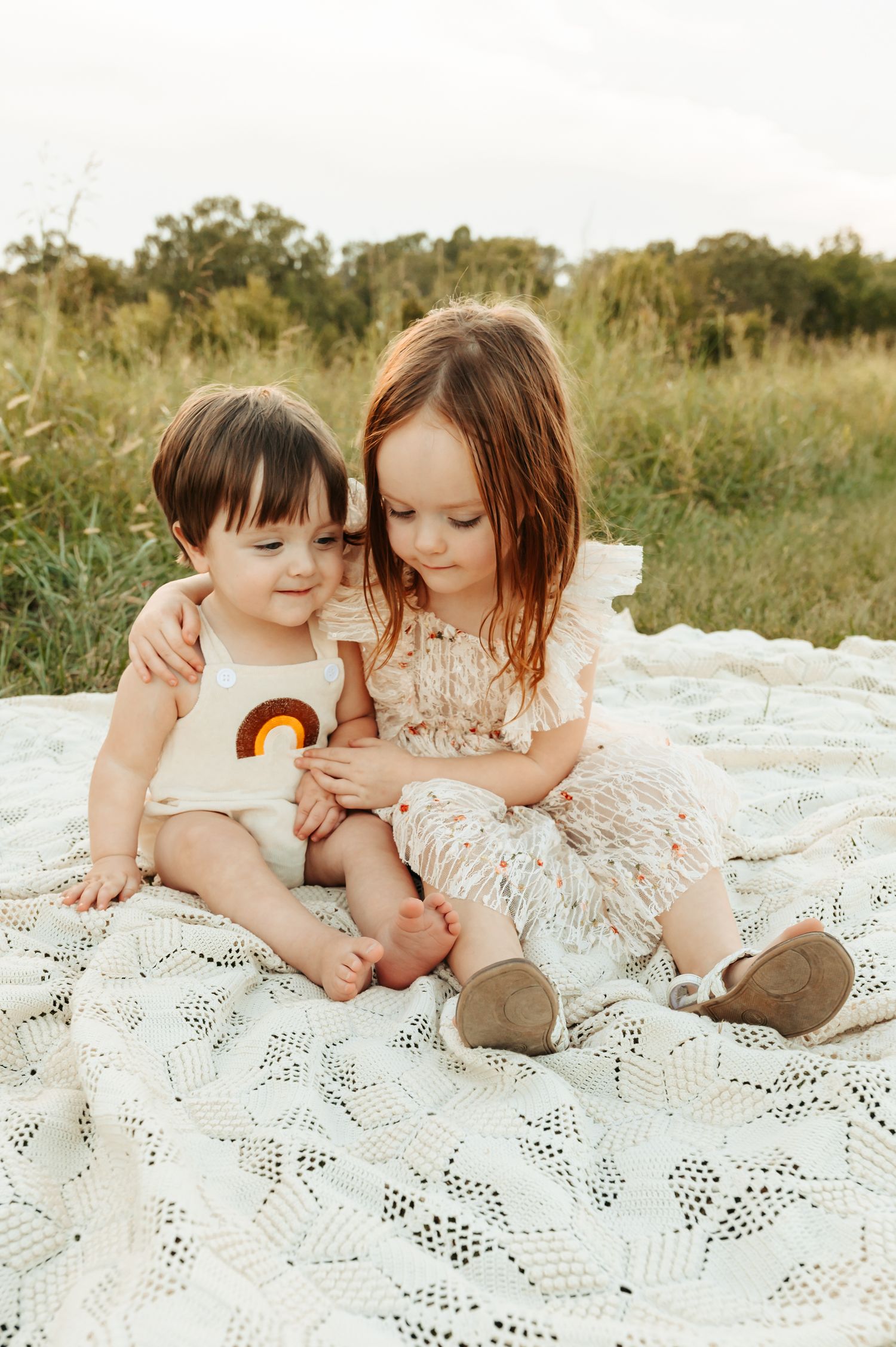 Tender moment captured outdoors on white lace blanket in natural setting.