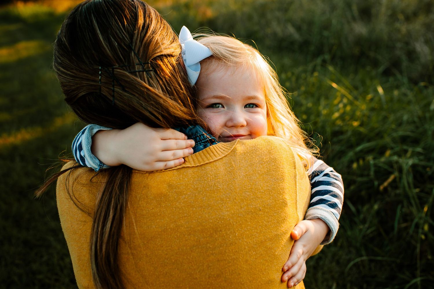A small child peeks over someone's shoulder while being held in a golden sunset.