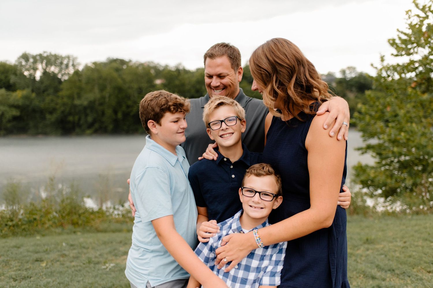 Family portrait taken outdoors by a misty lake during golden hour.