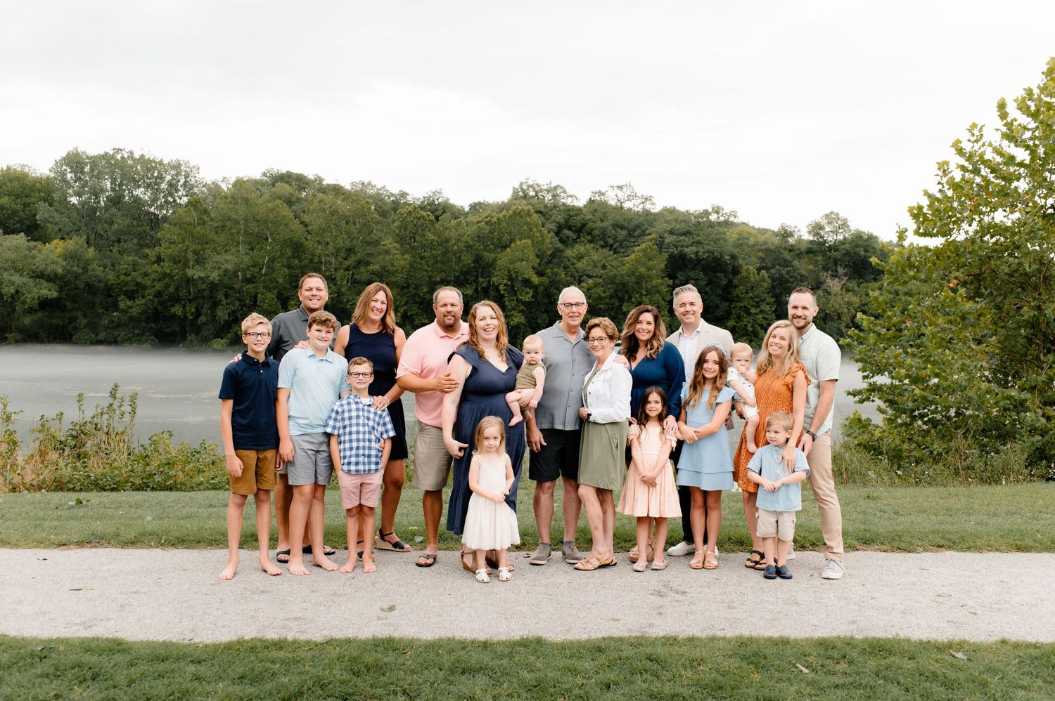 Large group photo of extended family gathered outdoors by a lake during summer.