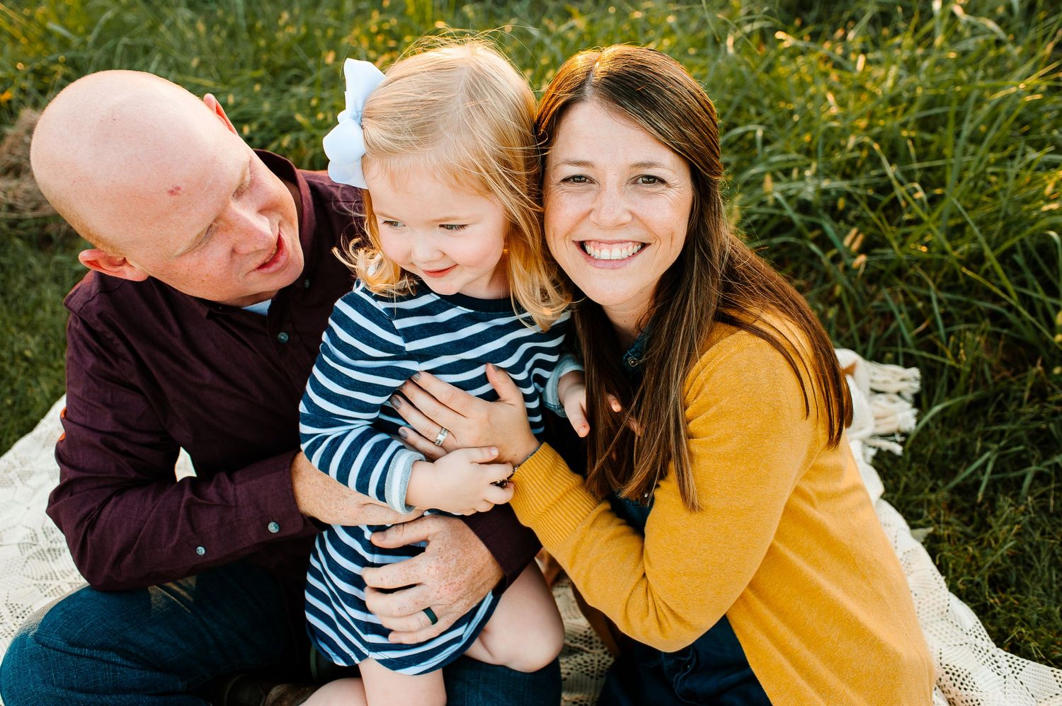 A happy family shares a joyful moment together while sitting on a white blanket outdoors.