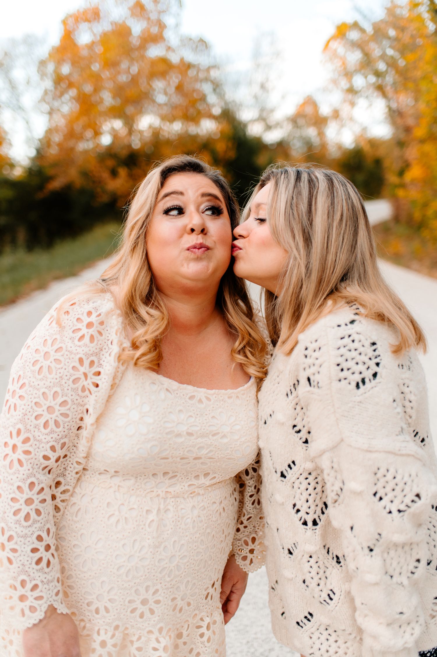 Friends in contrasting lace dresses share a playful moment on a rural road during fall.