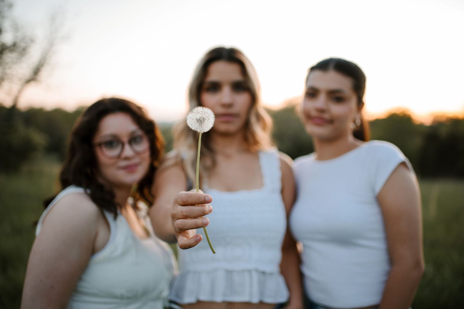 Three people standing close together in white outfits against sunset in outdoor field setting.