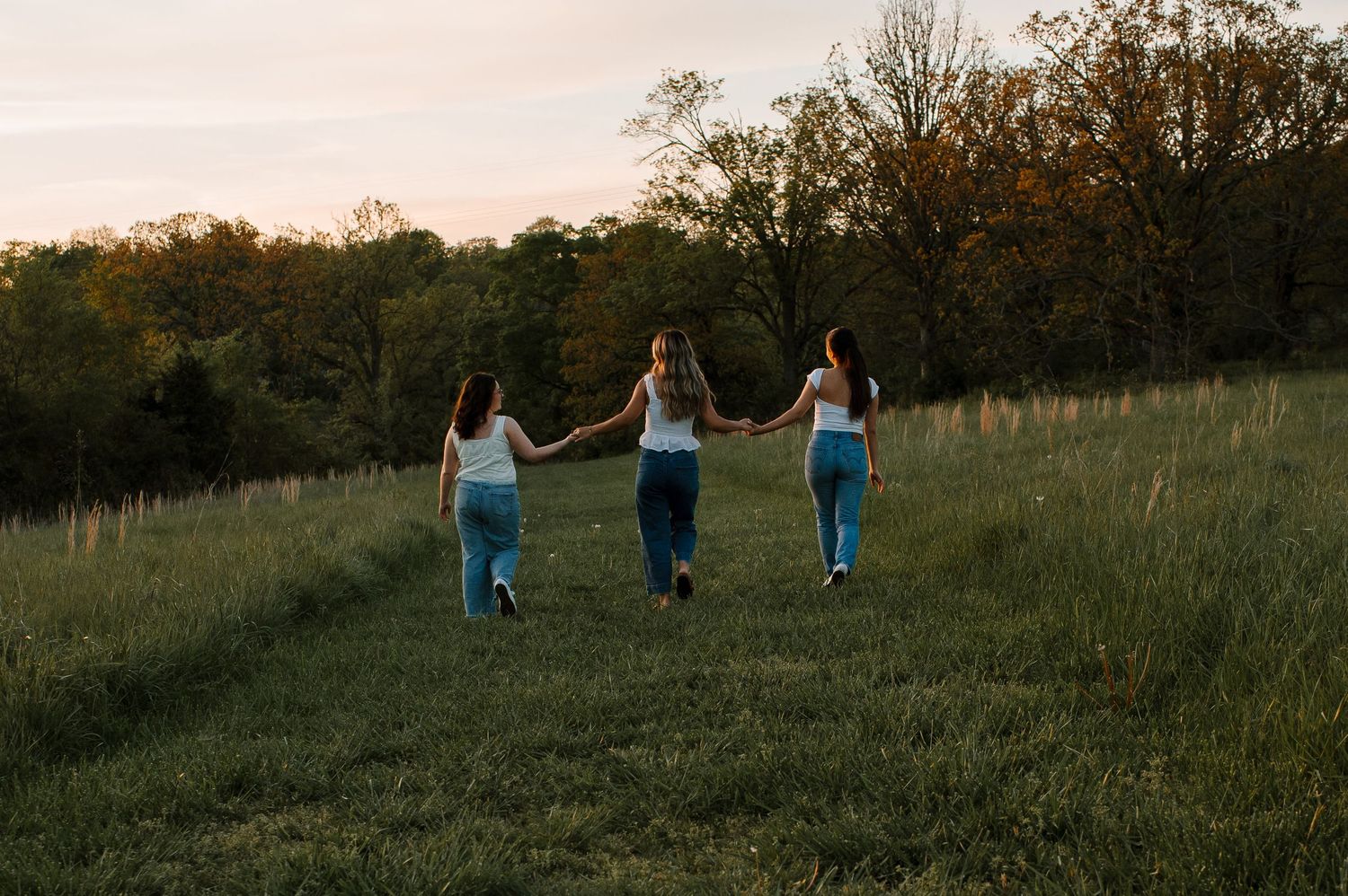 Three friends walking together in a grassy field at sunset, silhouetted against the golden sky.
