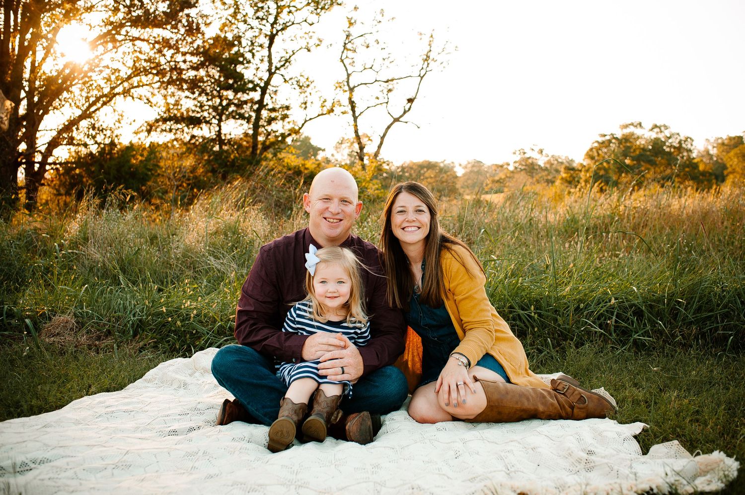A family sits together on a white blanket in a field during golden hour.