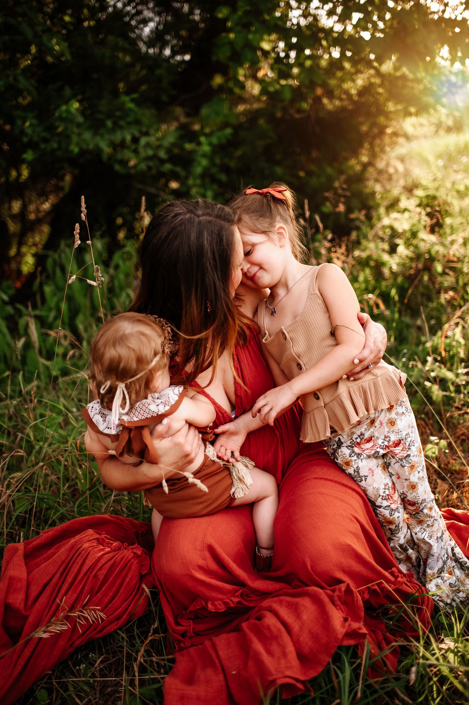 Intimate family moment captured in warm sunlight amidst tall grass and wildflowers.