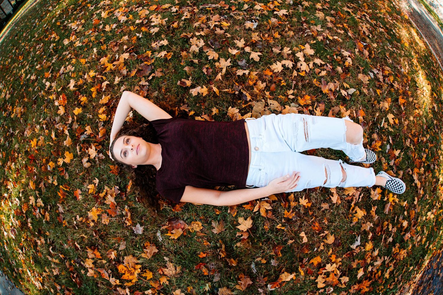 Fisheye view of someone lying on ground surrounded by fallen autumn leaves.