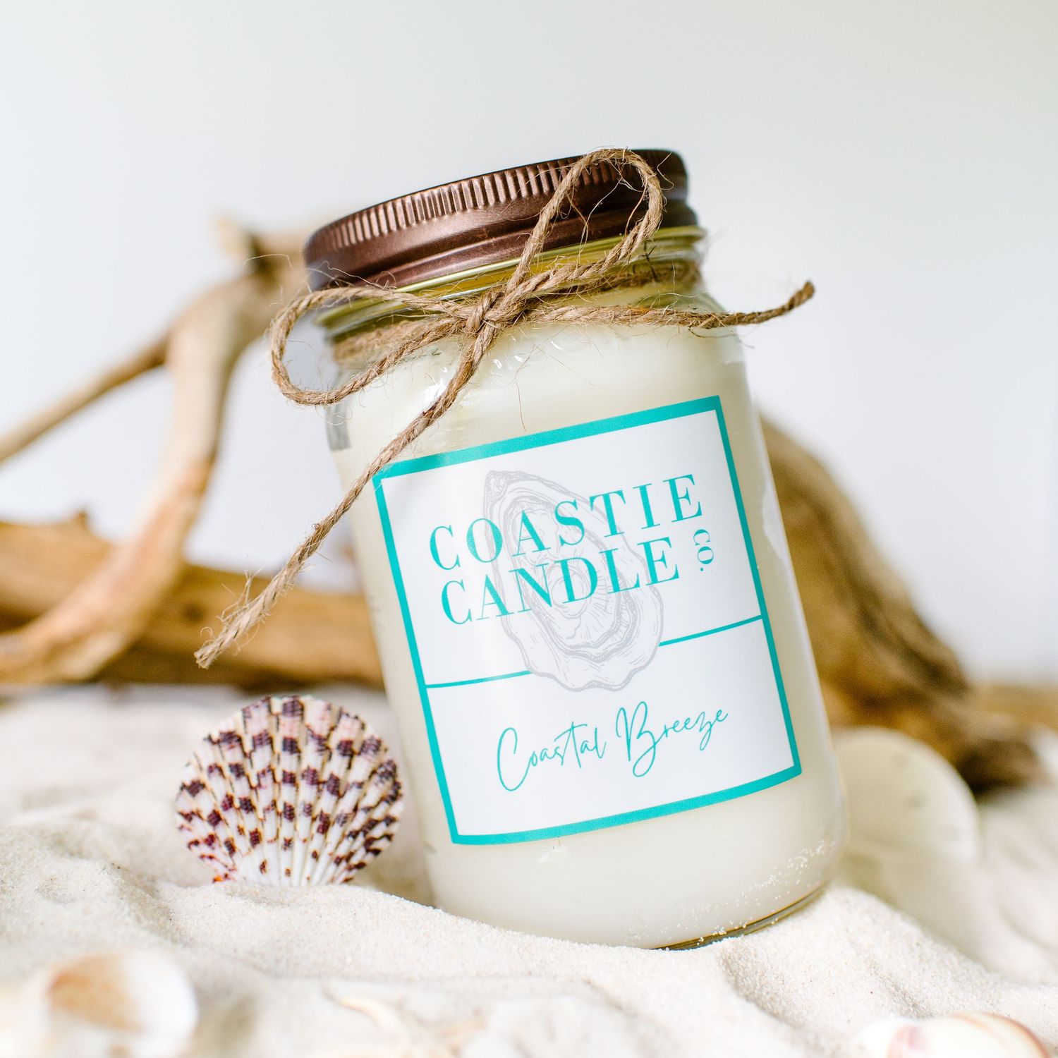 White candle in a mason jar with turquoise coastal label and twine bow, styled with dried botanical elements.