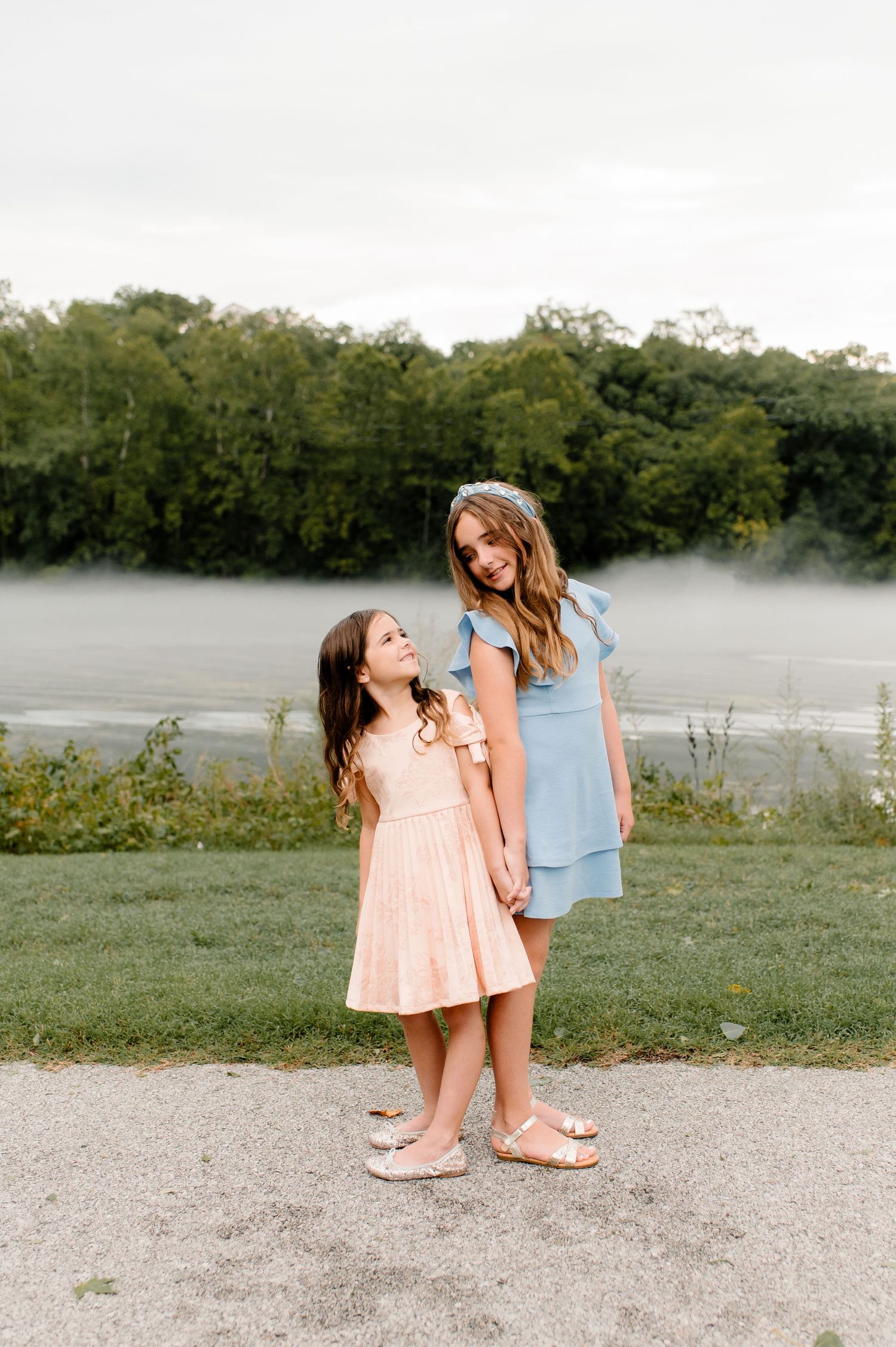 Two people in summer dresses standing by a misty lake during an outdoor photoshoot.