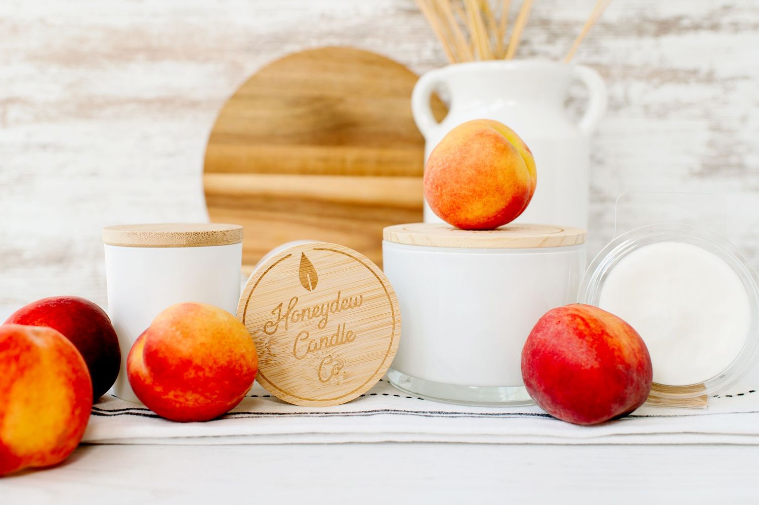 Fresh red and yellow peaches arranged with white ceramic mugs and a wooden cutting board on a rustic white surface.