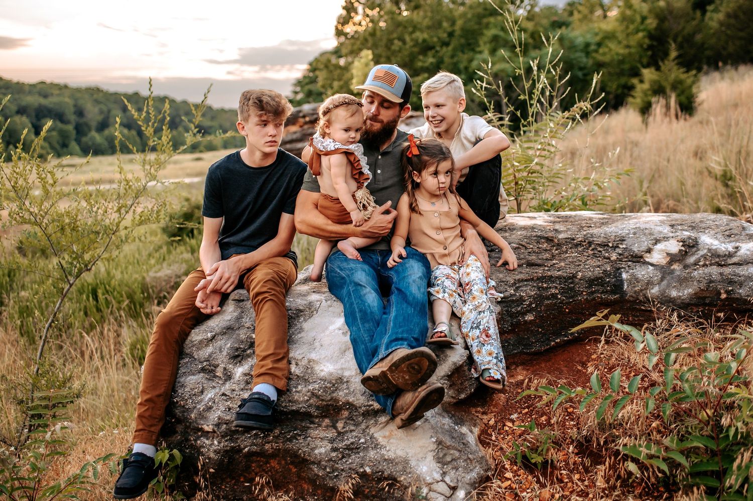 A relaxed outdoor family portrait showing people sitting together on a large rock formation.