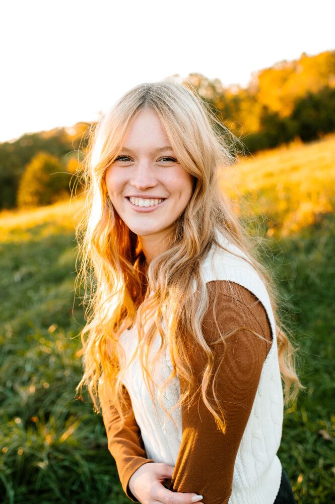 Portrait of a person in a cream and brown sweater against a golden autumn background.