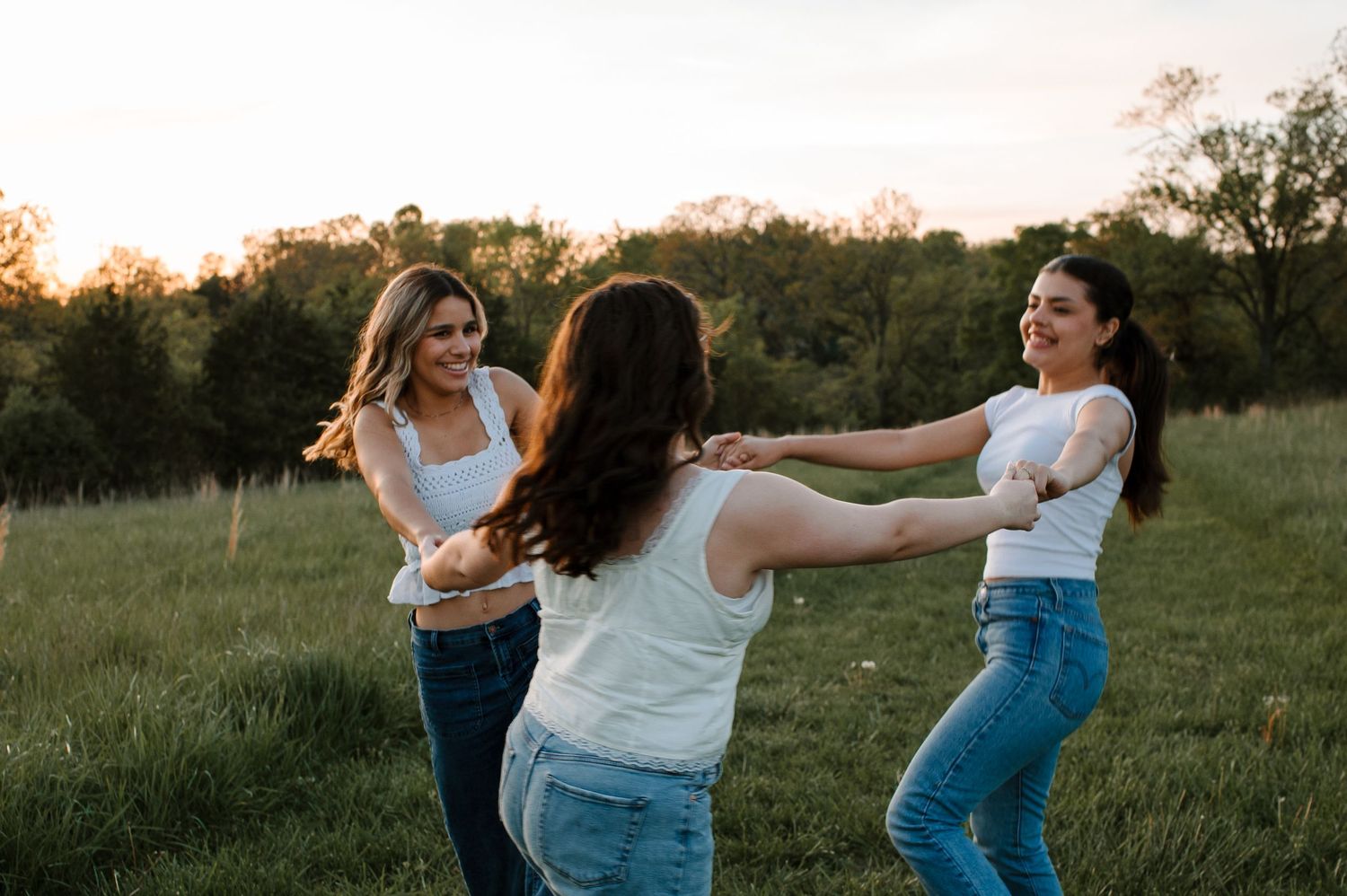 People holding hands and dancing in a circle on a hillside during golden hour.