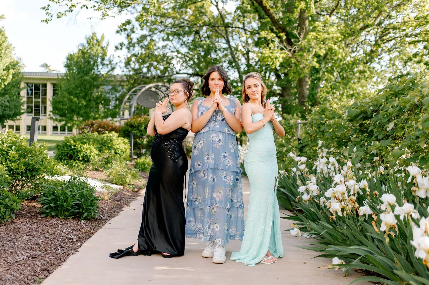 Wedding party members walk along a garden path in pastel blue dresses and black suits.