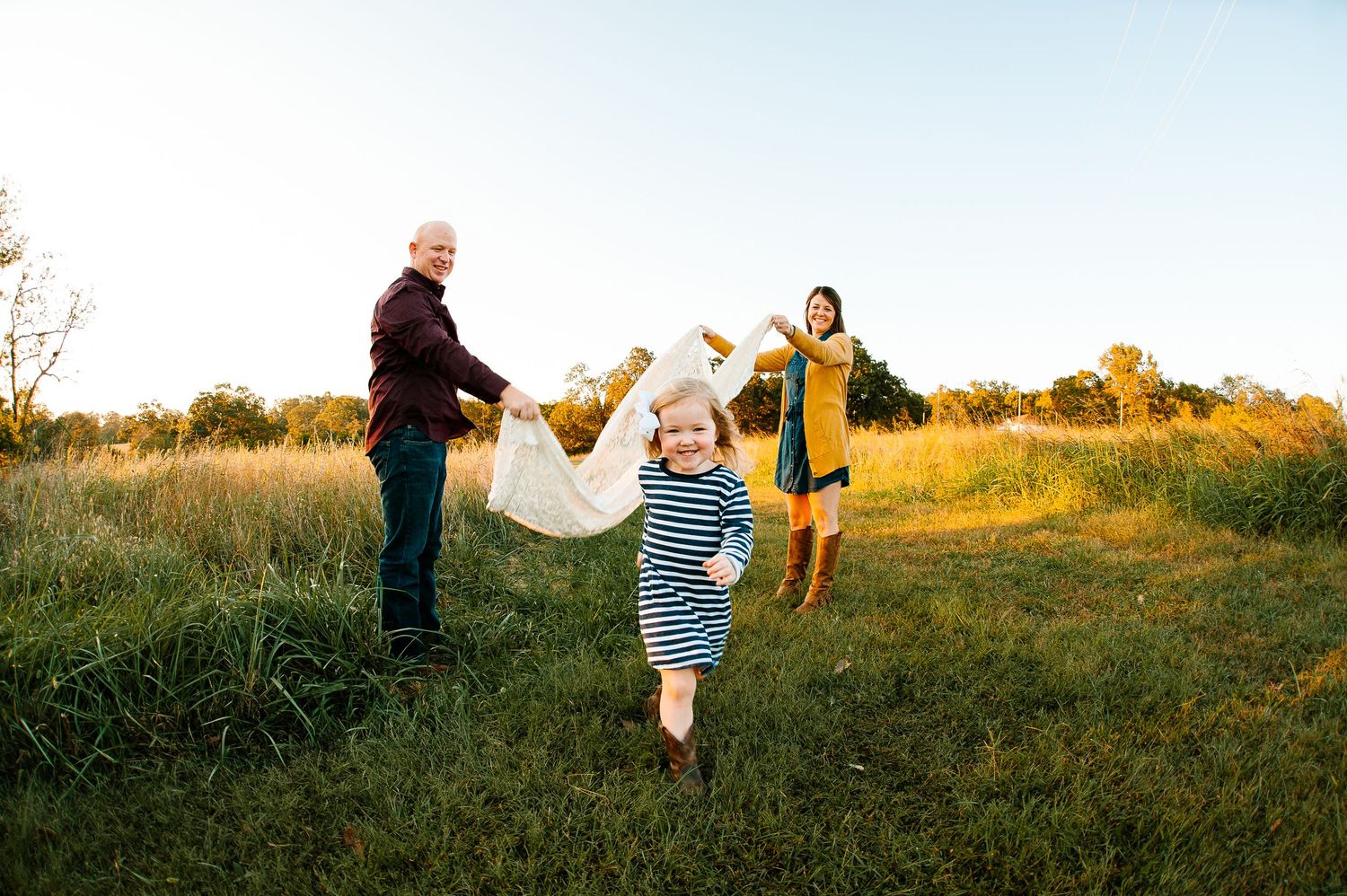 Playful outdoor family scene at sunset in a grassy field with yellow wildflowers.