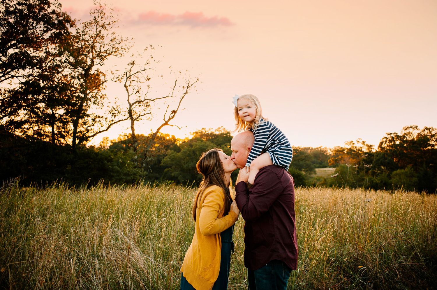 Sunset family portrait in a golden field with tall grass and trees in background.