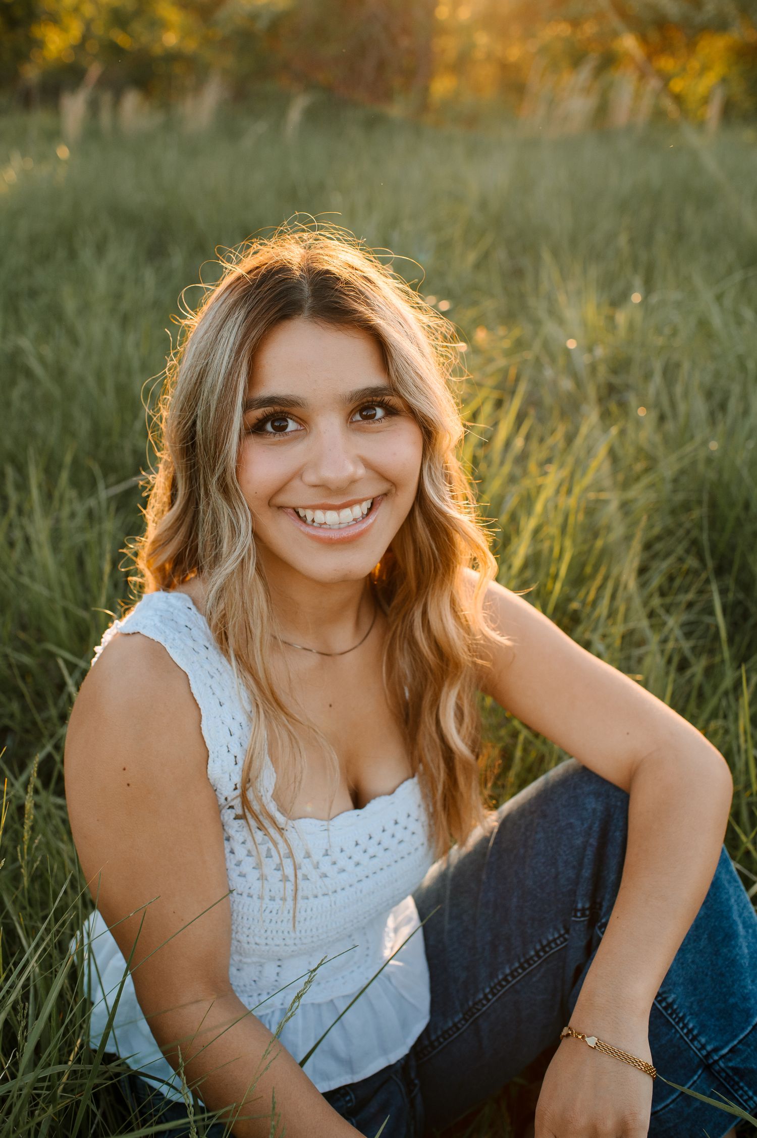 Golden sunset portrait session in tall grass with white lace top and natural lighting creating a warm summer glow.