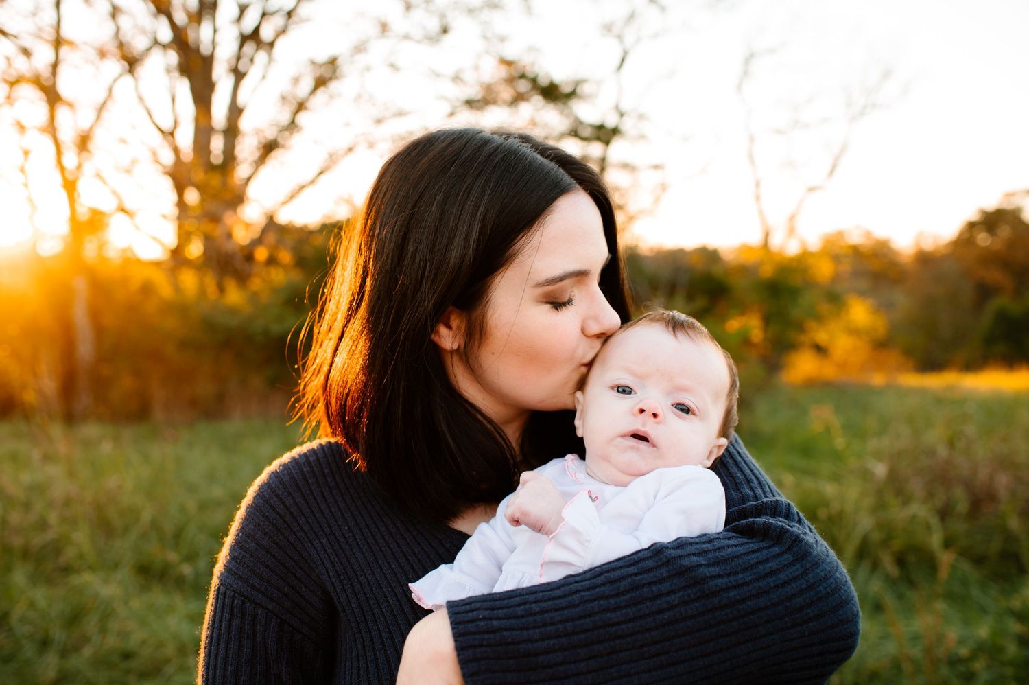 A tender moment captured at sunset as a parent holds an infant wrapped in a blanket.