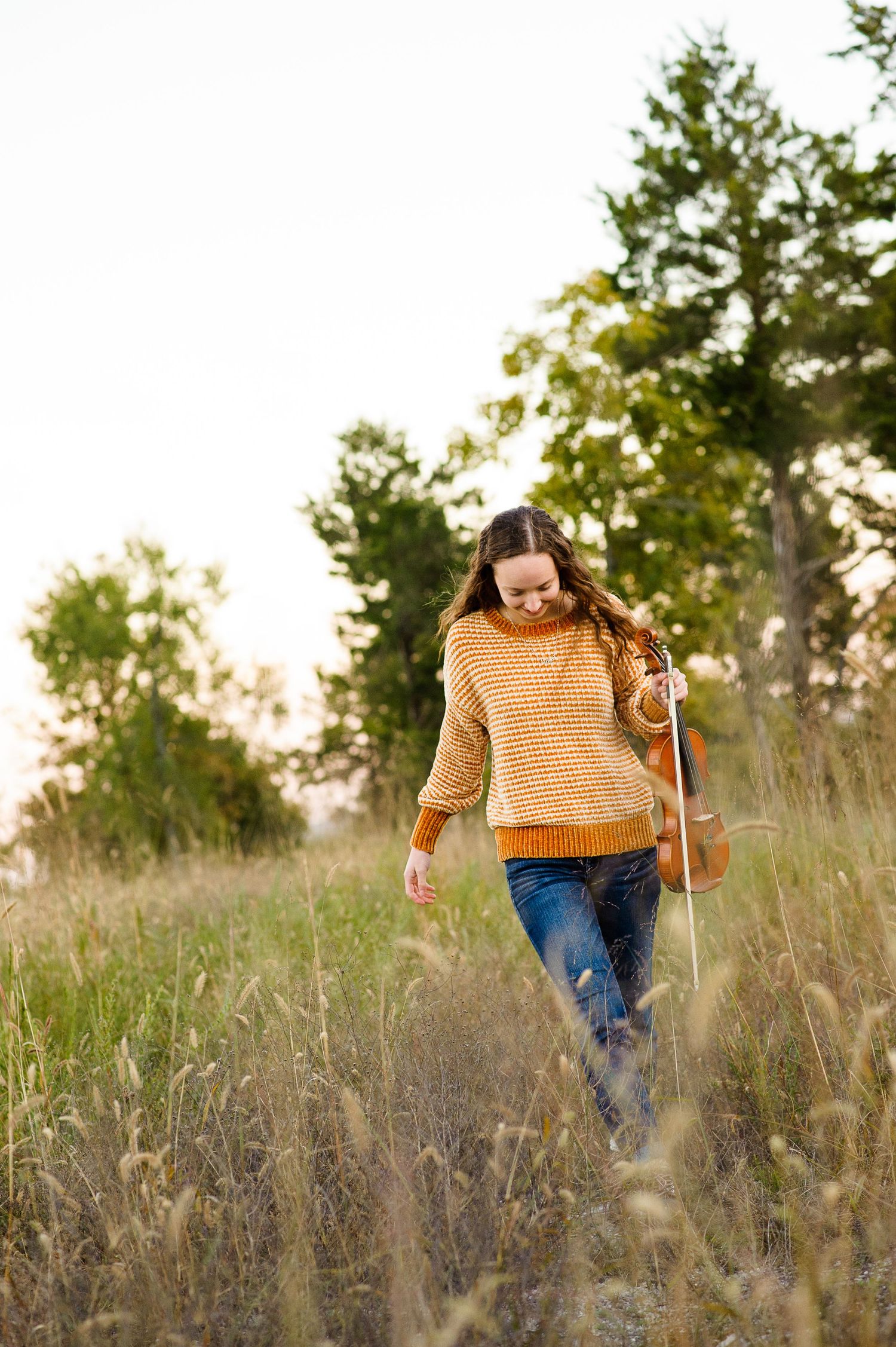 Person walking through tall grass wearing mustard yellow sweater at sunset.