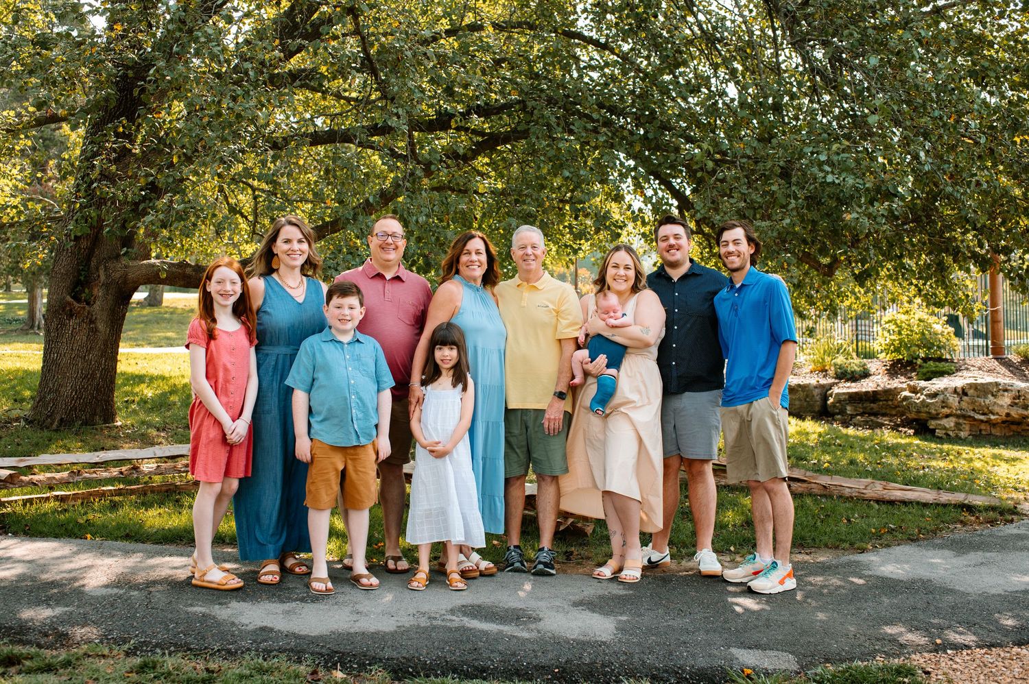 Large family group portrait outdoors under tree canopy.