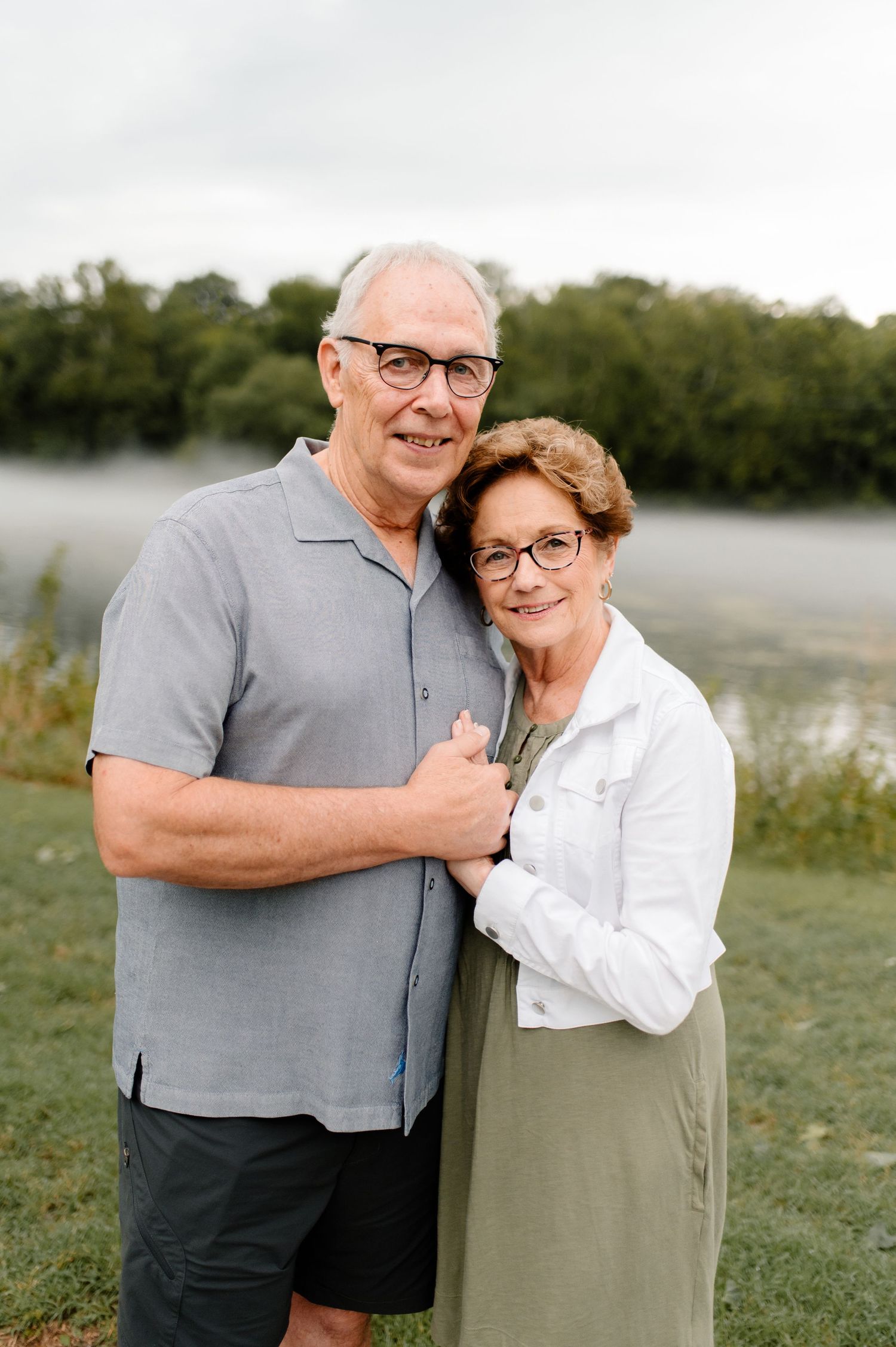 Outdoor portrait of a couple by a misty lake wearing casual attire.