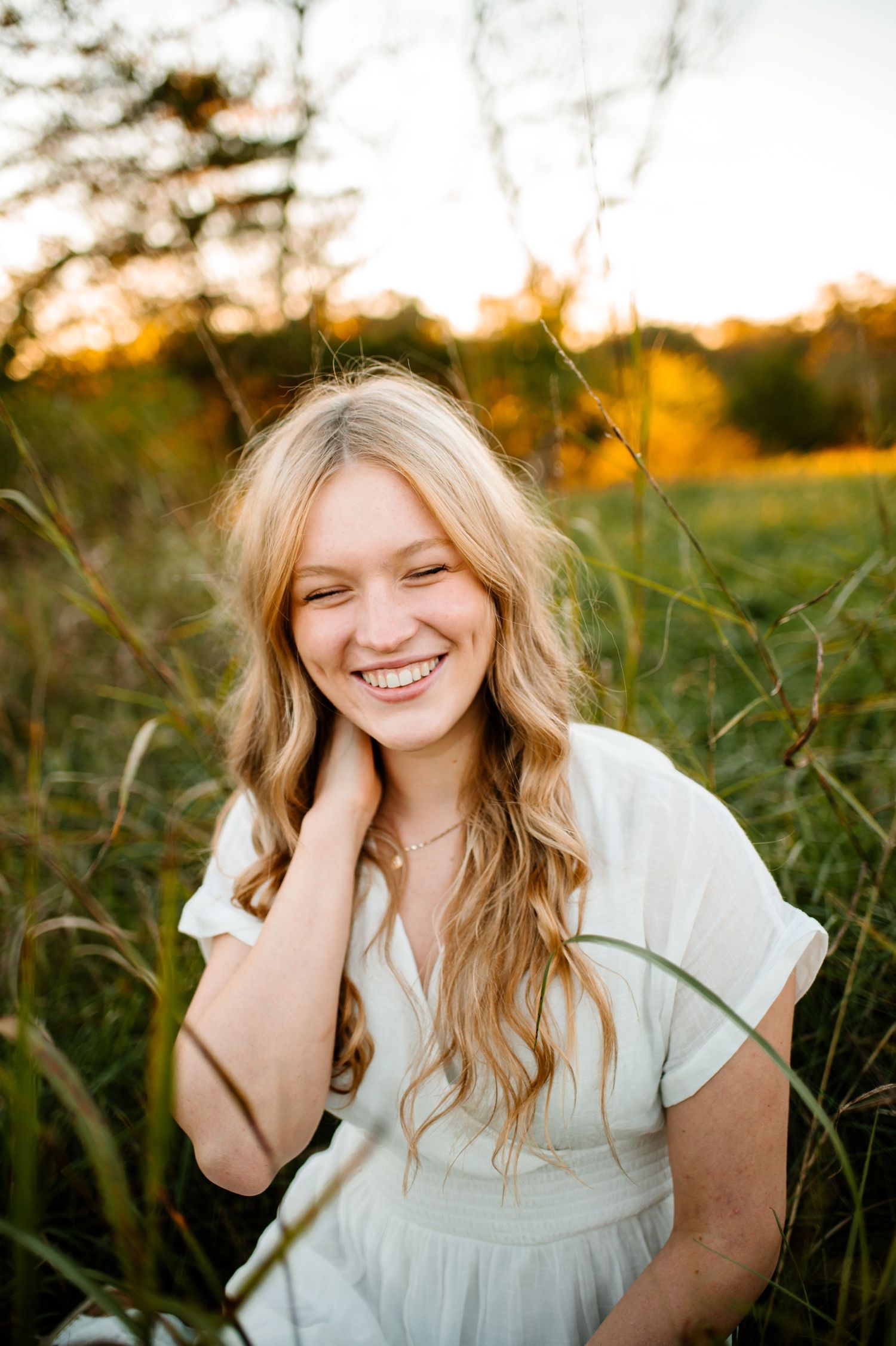 Outdoor portrait in white dress amid tall grass at sunset.