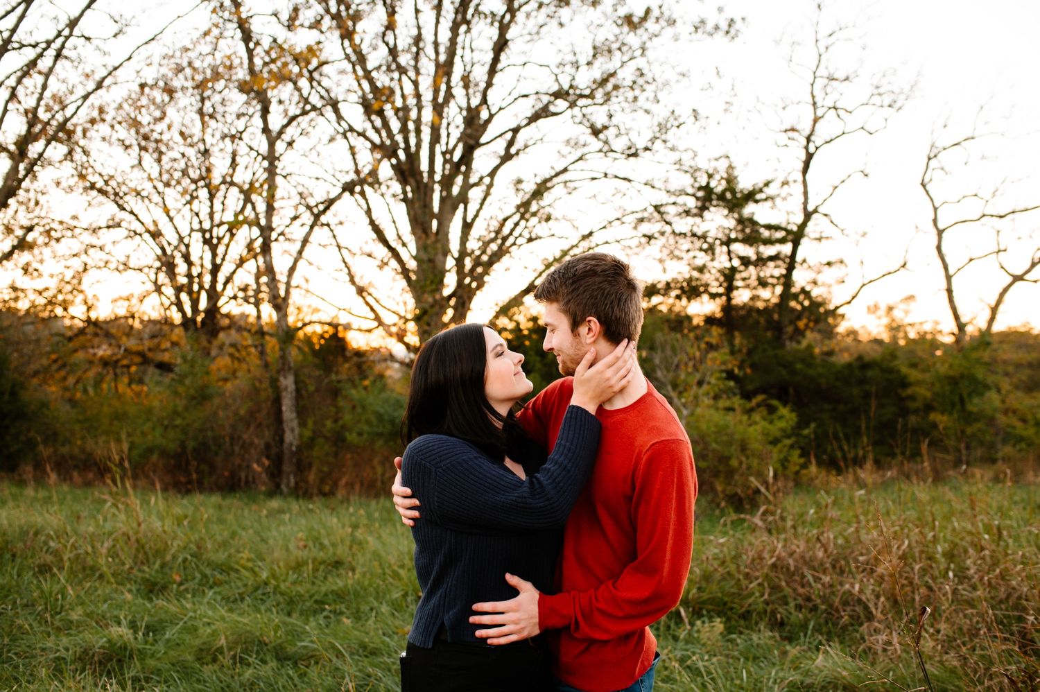 A couple sharing an intimate moment in a sunlit meadow at dusk.