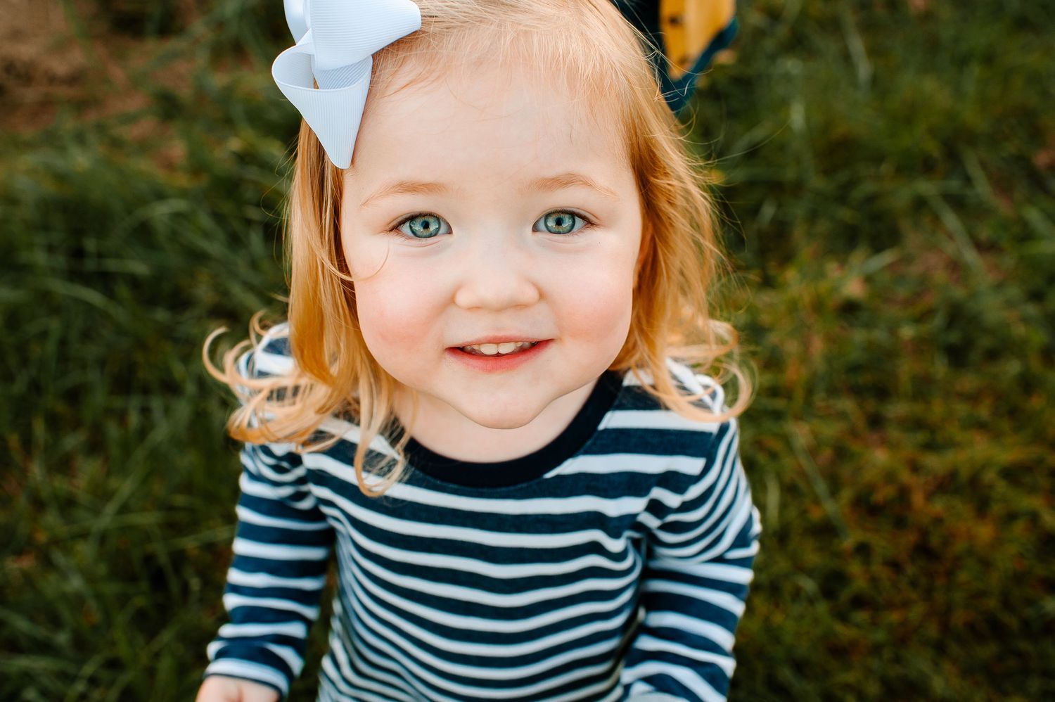 Close-up outdoor portrait of a child in striped shirt and white bow with natural background.