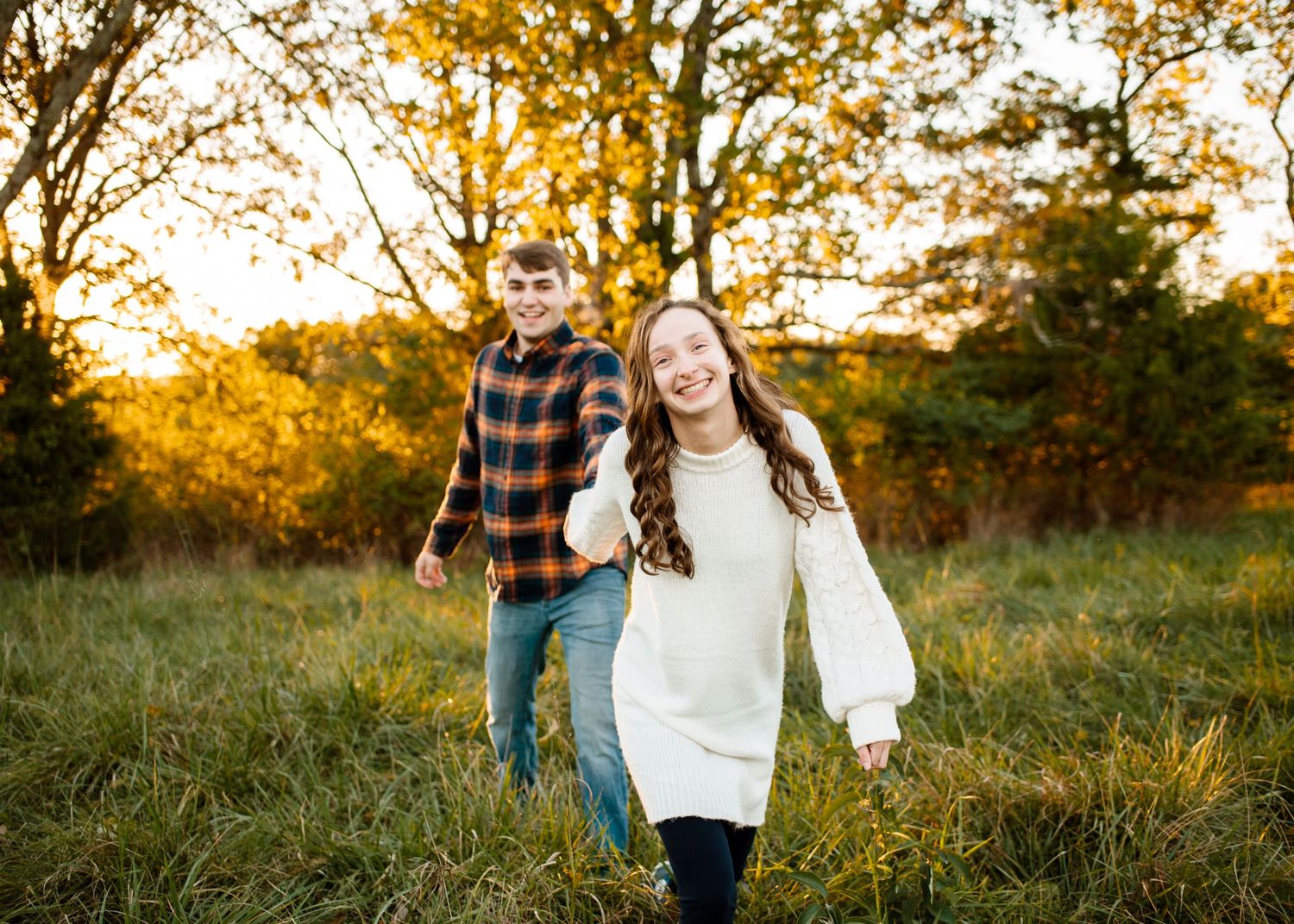 Two people walking through a golden autumn field during sunset.