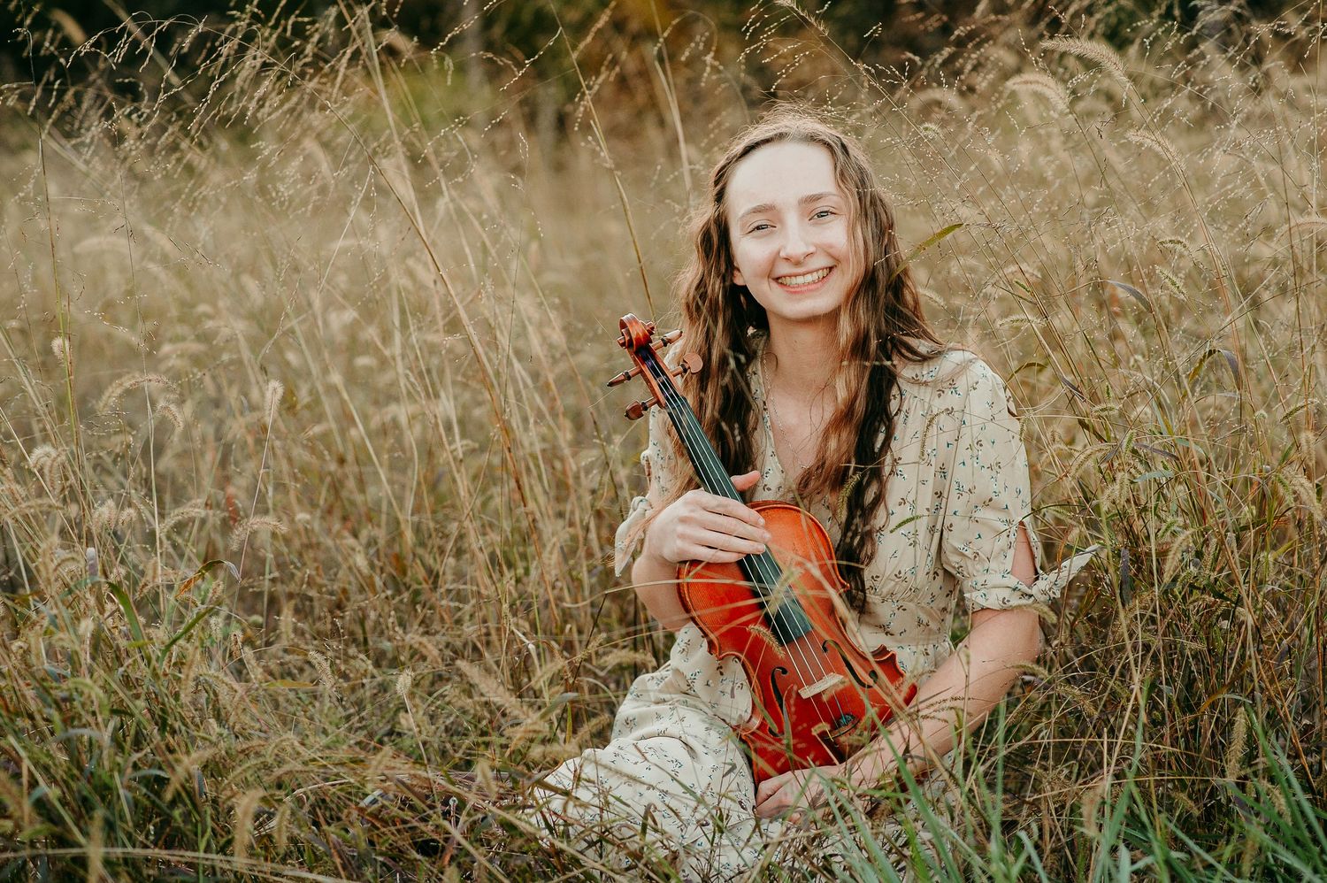 Portrait in lace dress holding violin in rustic field setting.