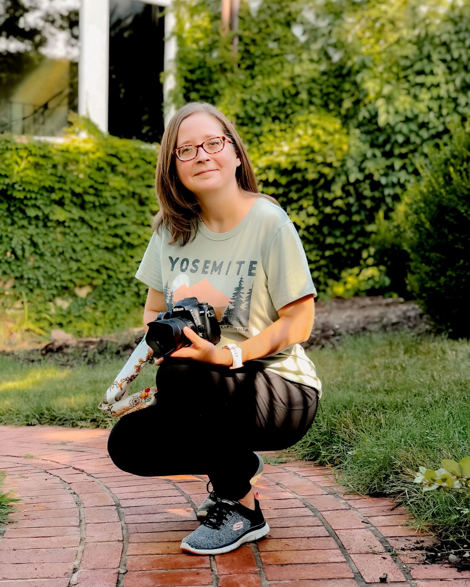 Photographer wearing a Yosemite t-shirt crouches with camera on brick pathway.