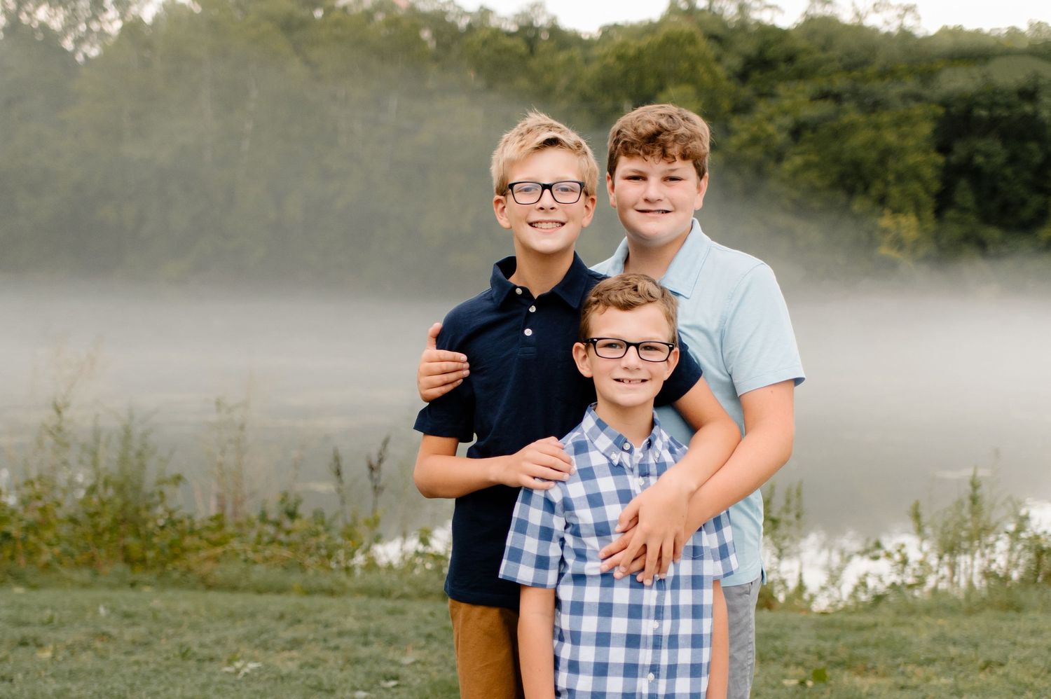 Three people posing together outdoors with a misty lake in the background.