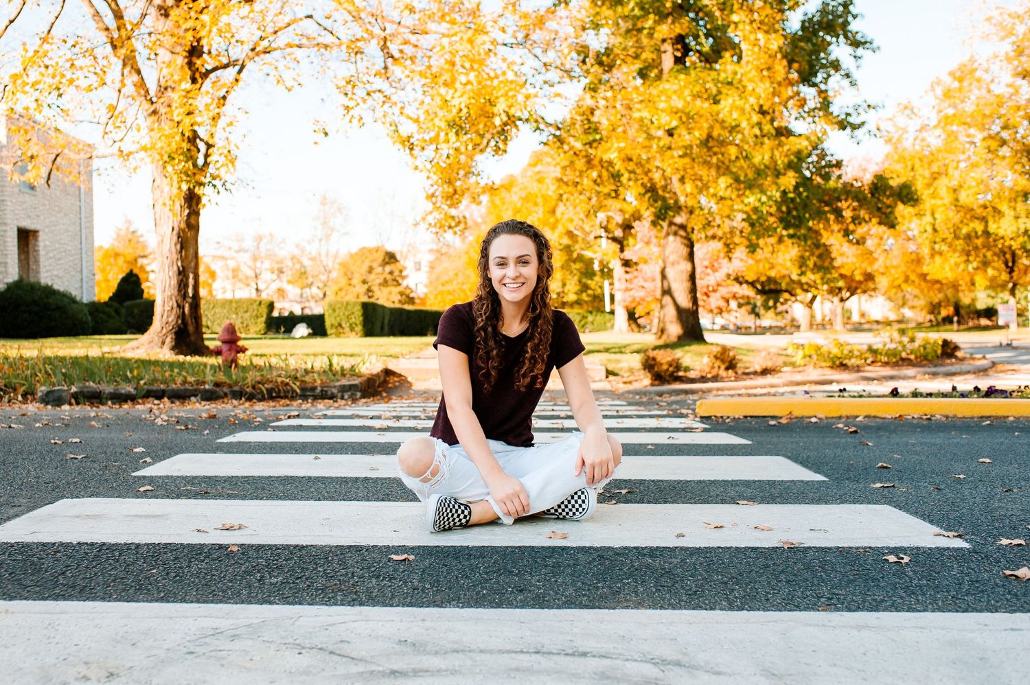 A person sits cross-legged on a crosswalk surrounded by golden autumn trees.