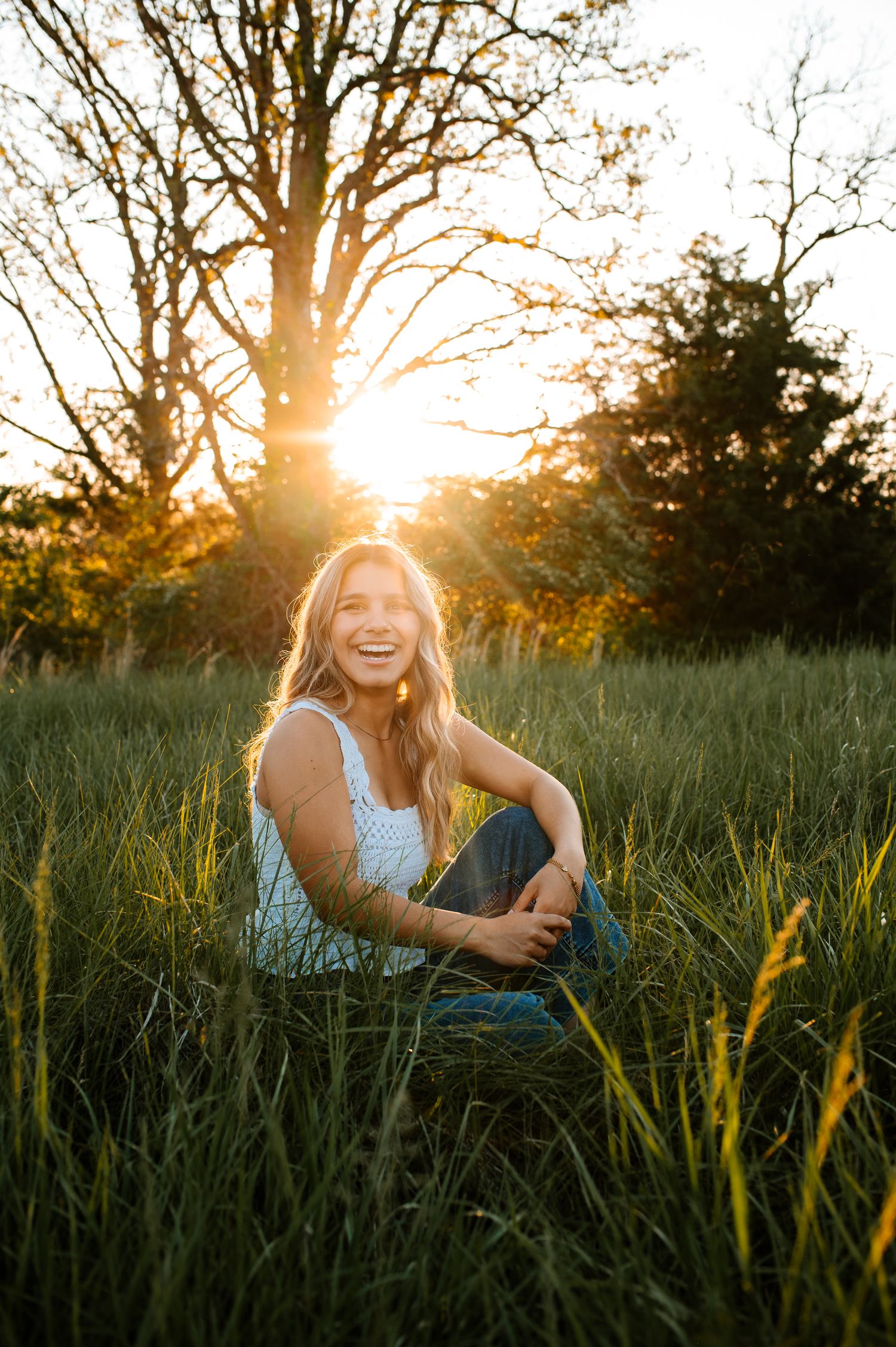 A joyful portrait in a grassy meadow at golden hour with sunlight streaming through trees in the background.