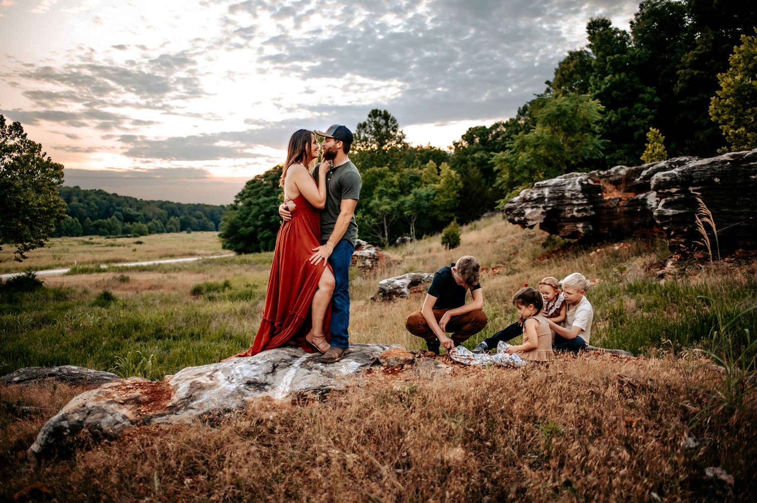 Multiple people enjoying a scenic sunset moment on a grassy hilltop with rocks.