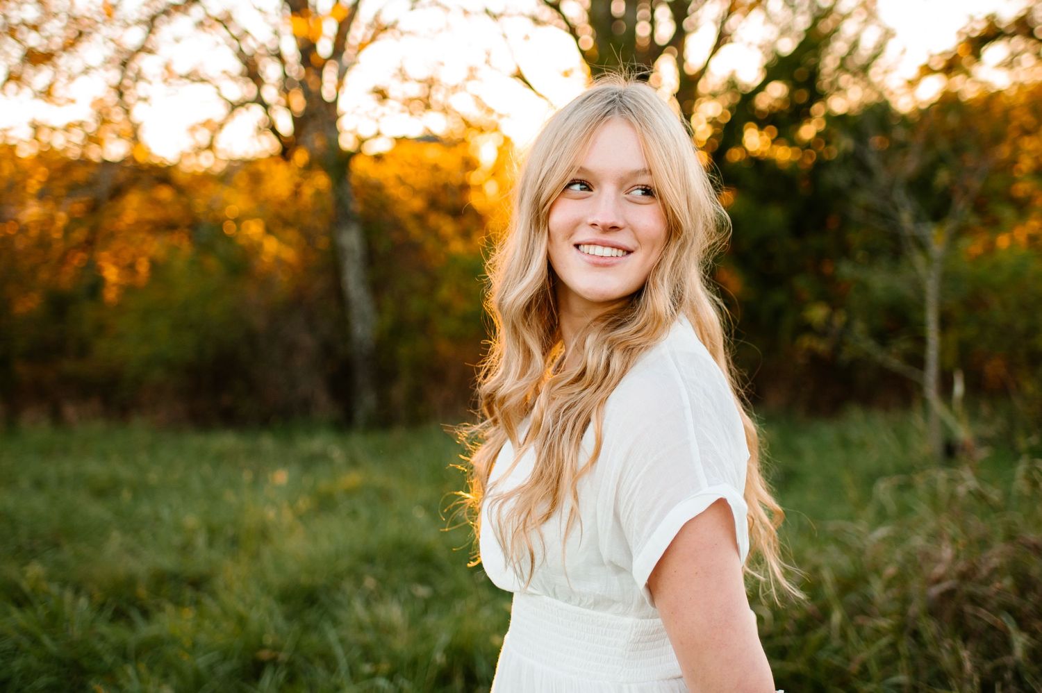 Golden hour portrait in white dress against natural outdoor setting.