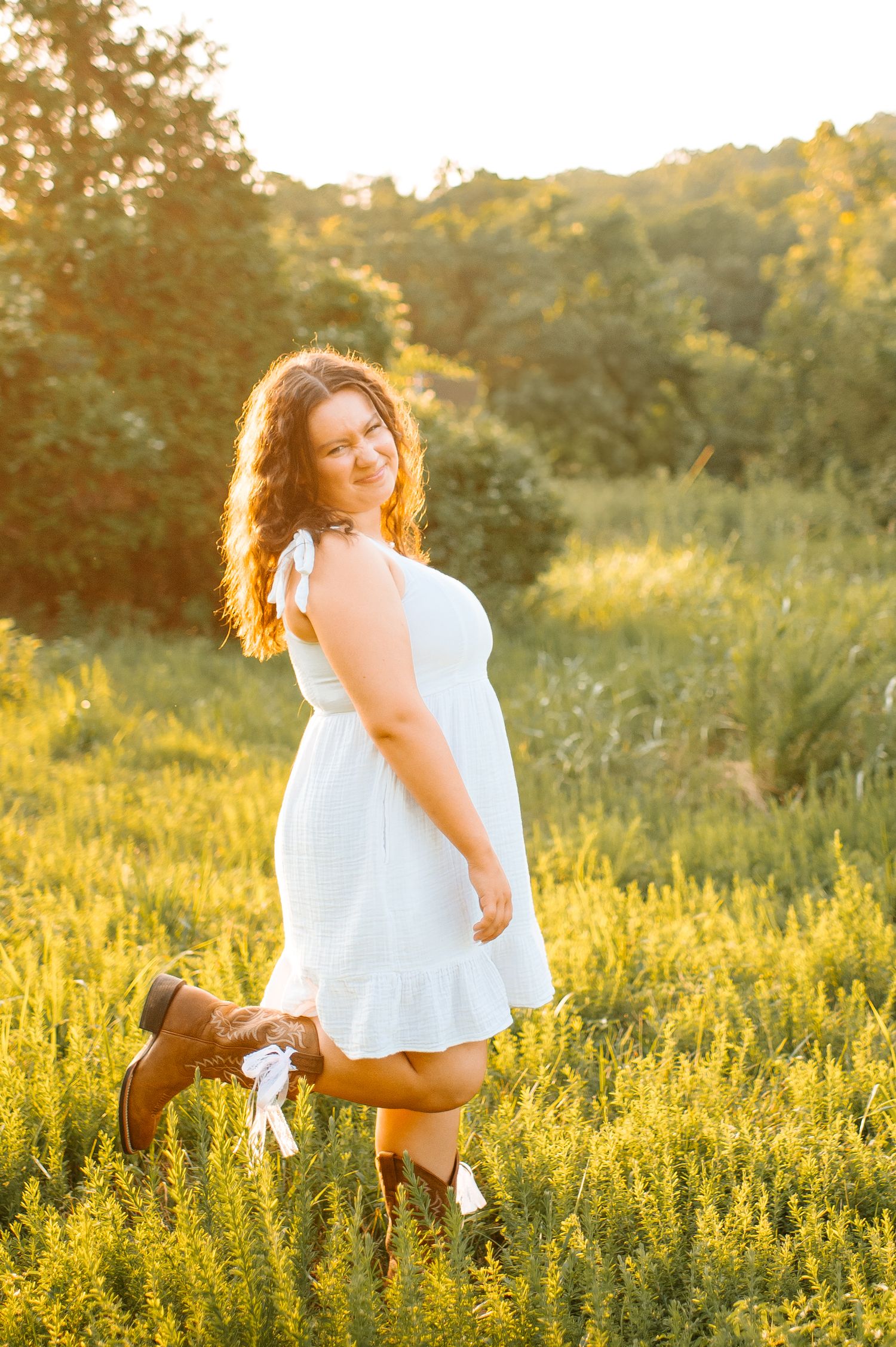 A person in a white dress twirls playfully in a golden sunlit meadow during sunset.